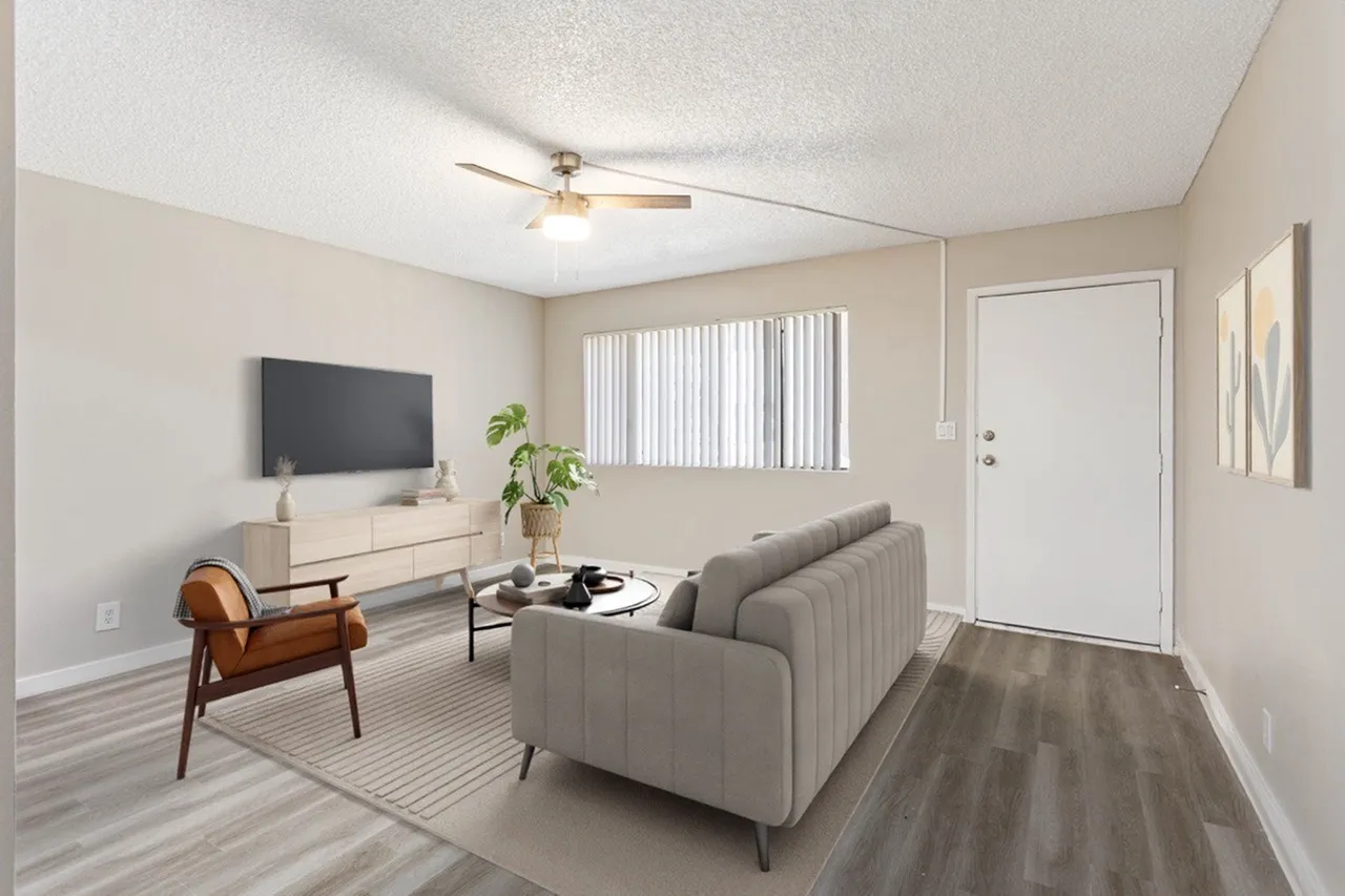 Living room with wood-style plank flooring, ceiling fan, gray sofa, leather accent chair, TV mounted on cream console