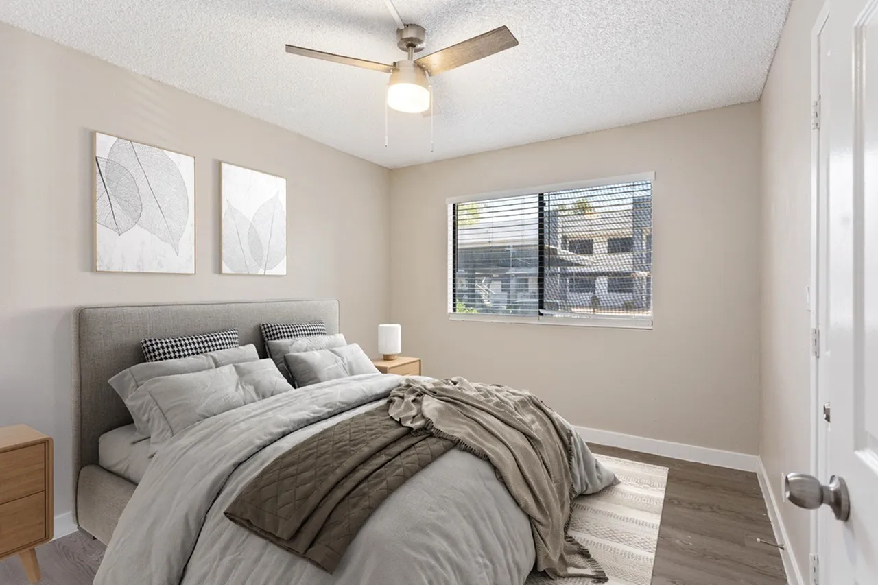 Primary bedroom, gray upholstered bed, wood-style plank flooring, ceiling fan with light, windows with blinds