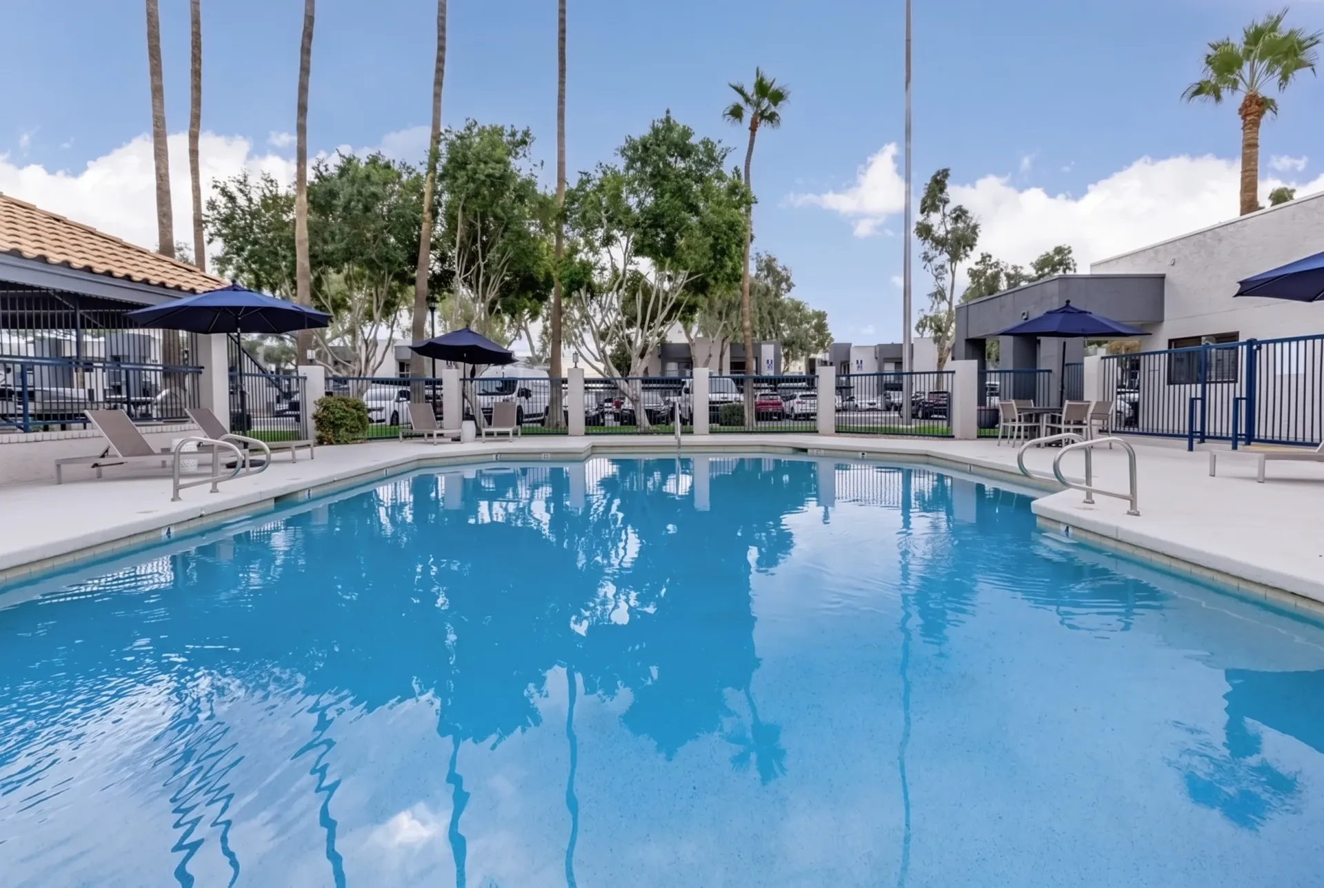Resort-style swimming pool, clear blue water, palm trees, lounge chairs, umbrellas, buildings