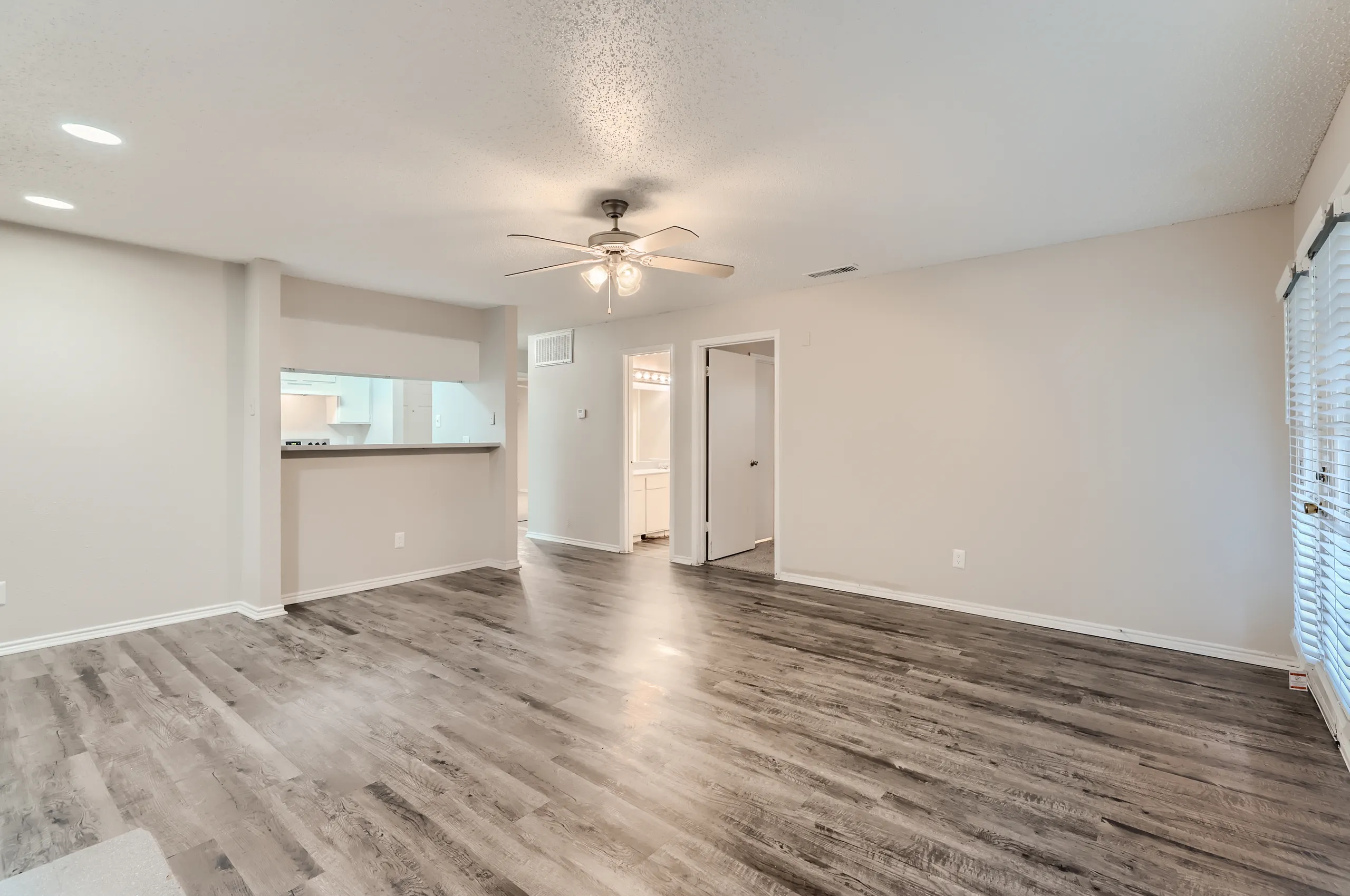 Living room with wood-look flooring and view into hallway and kitchen