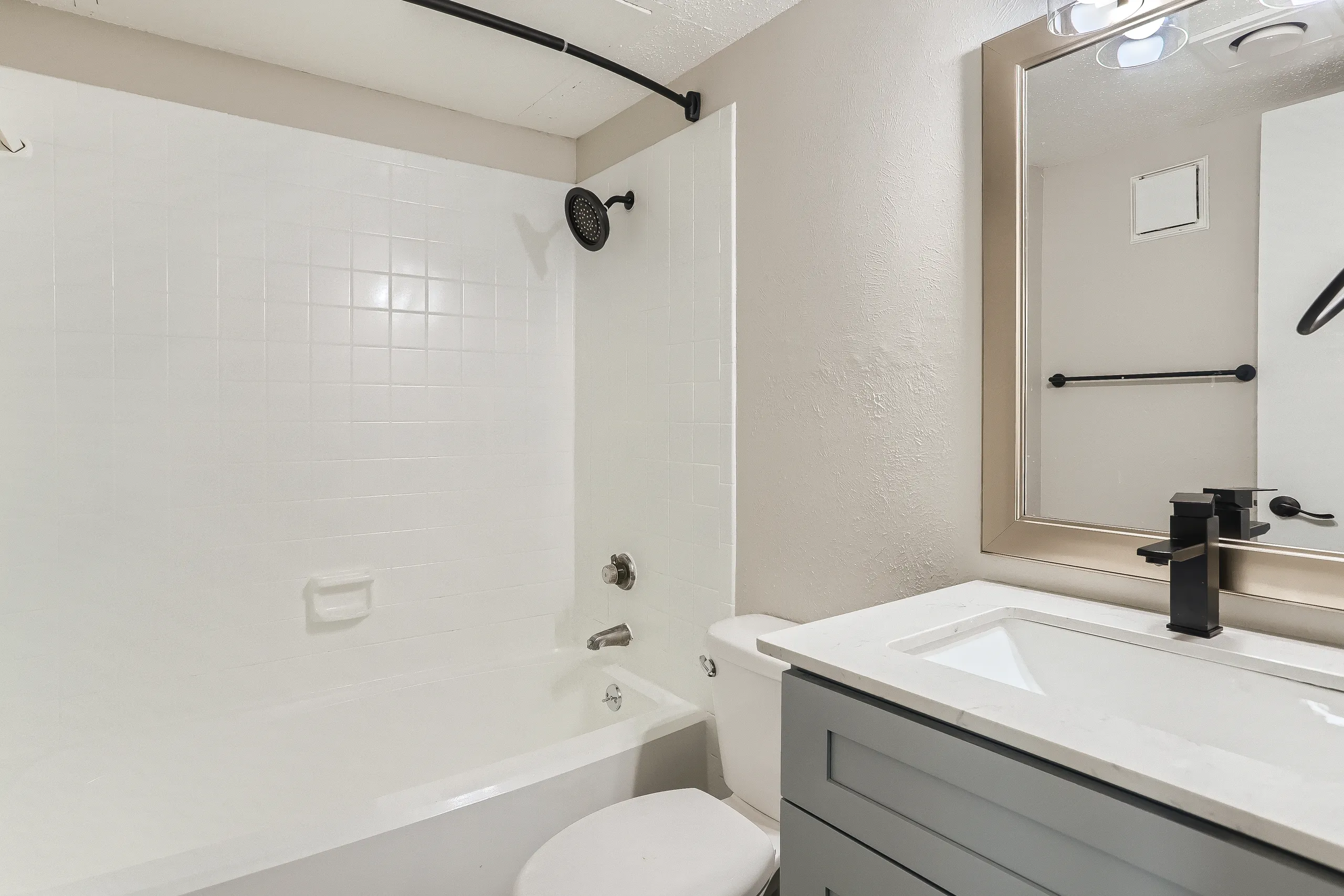 Renovated bathroom with quartz vanity, matte black fixtures, and tub-shower combo