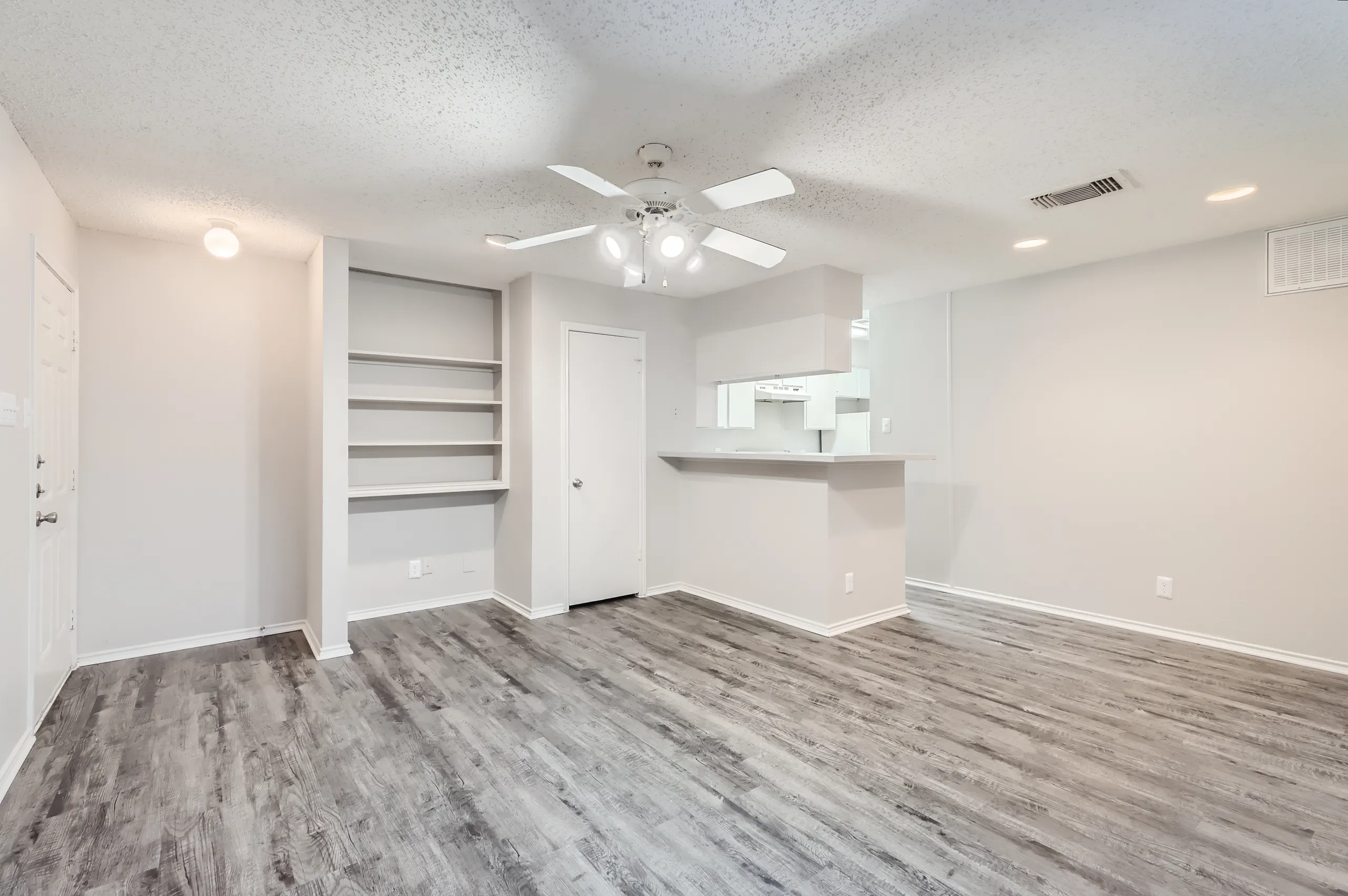 Apartment living room with wood-look flooring, ceiling fan, and open kitchen pass-through