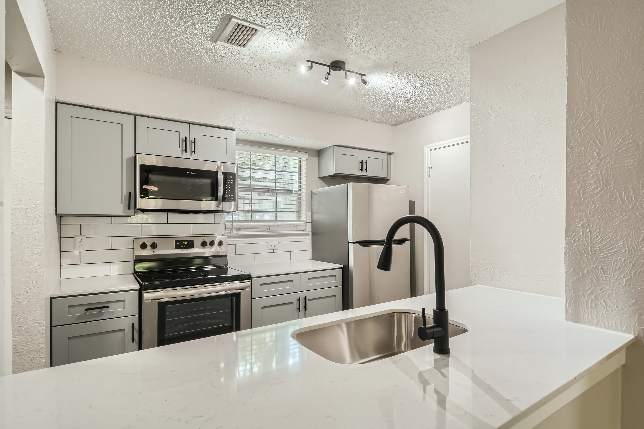 Renovated kitchen with gray cabinetry, quartz counters, and stainless appliances
