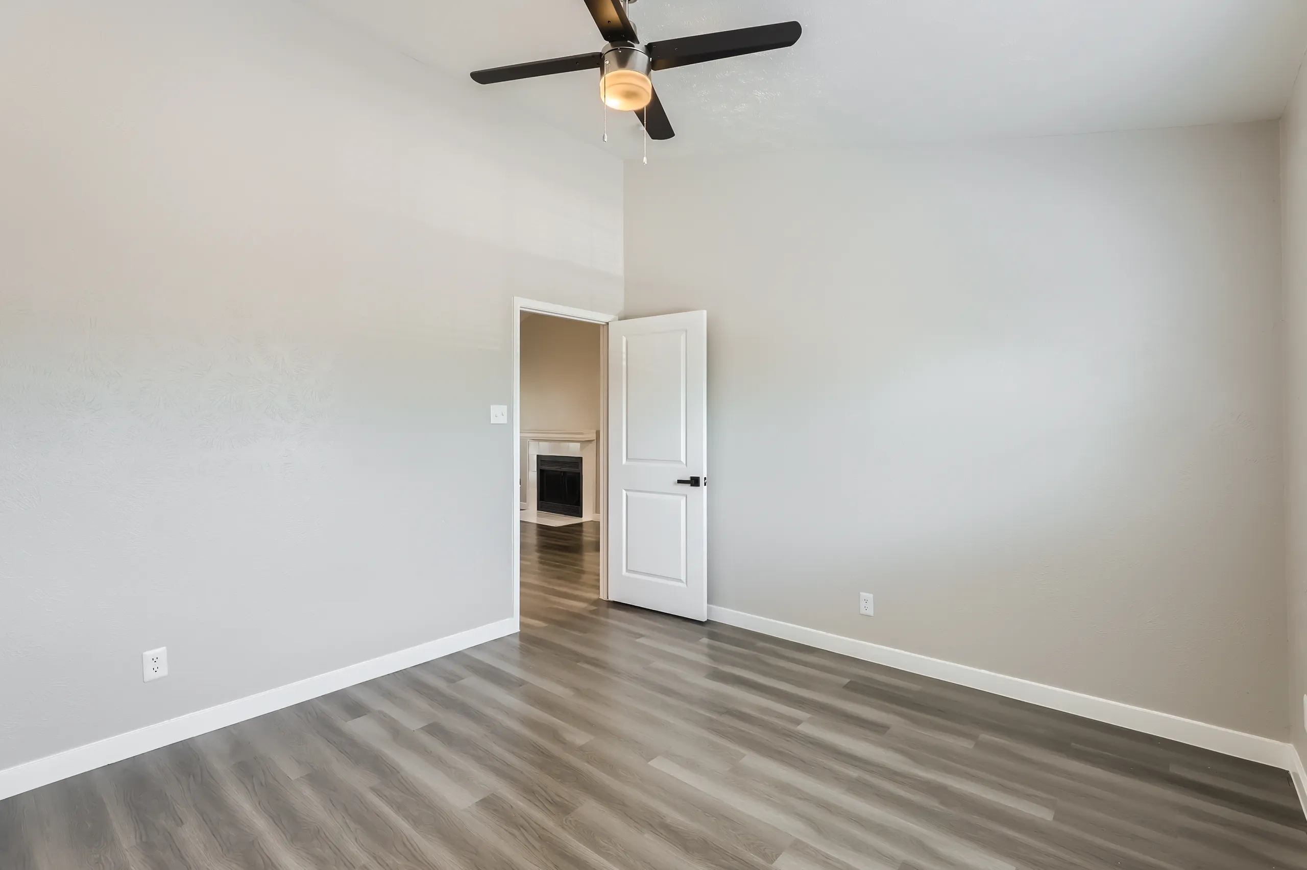 Primary bedroom with wood-look flooring and view into living room fireplace