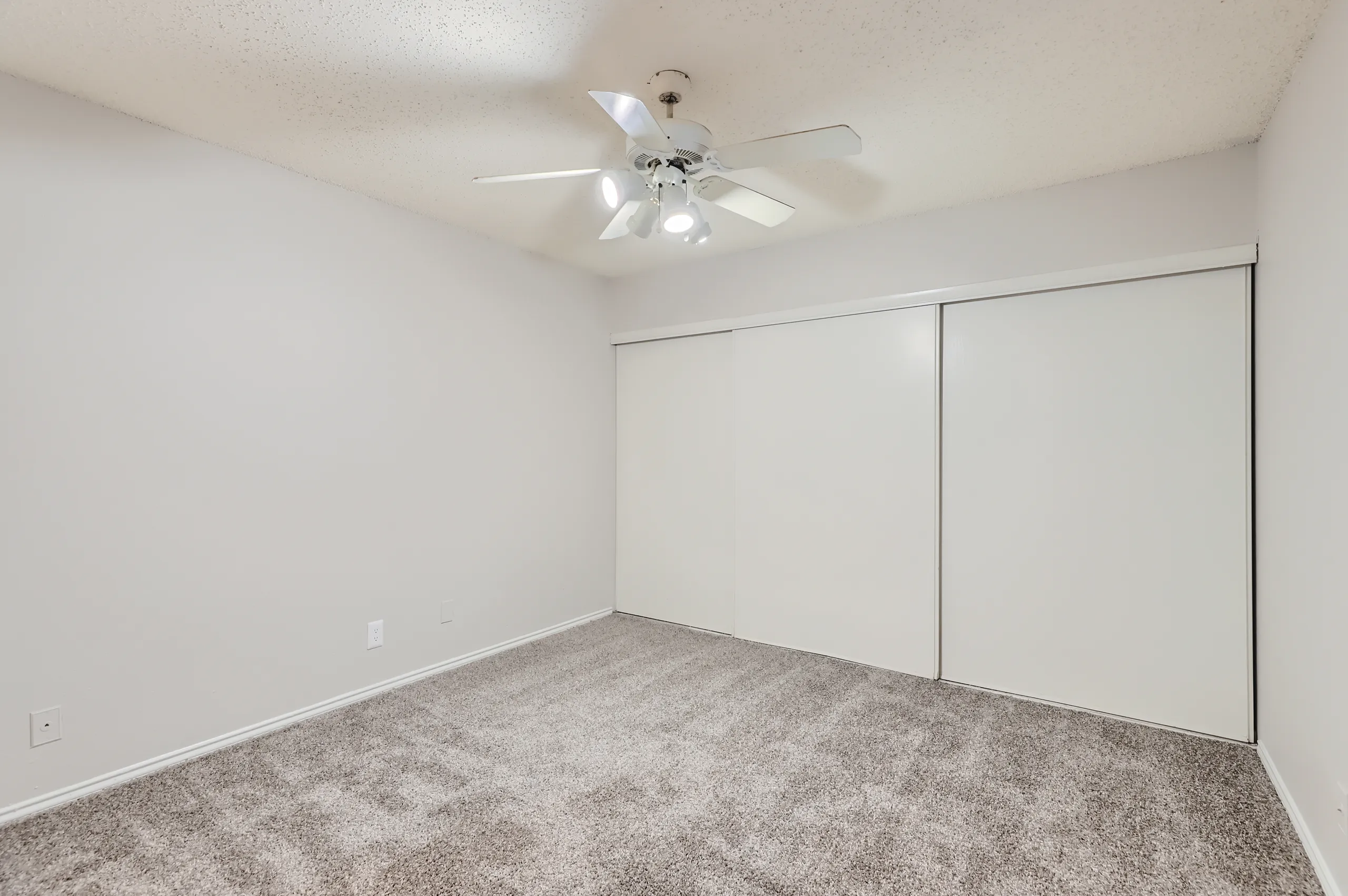 Carpeted primary bedroom with ceiling fan and sliding closet doors
