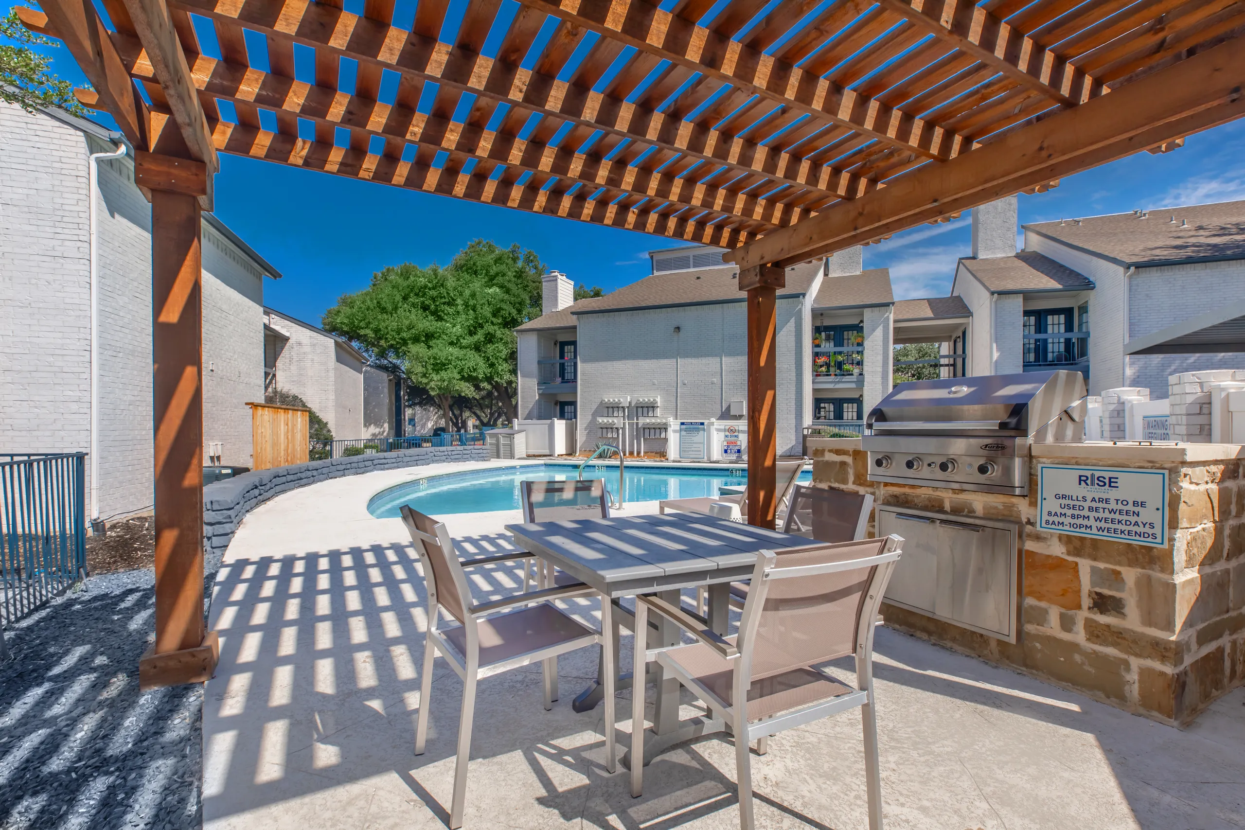 Outdoor grilling station under a wooden pergola near the pool