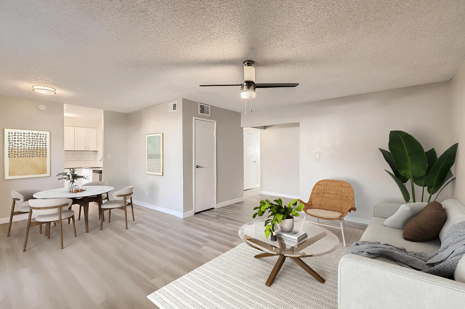 Open living area, wood-style plank flooring, ceiling fan, dining table with chairs, potted plant
