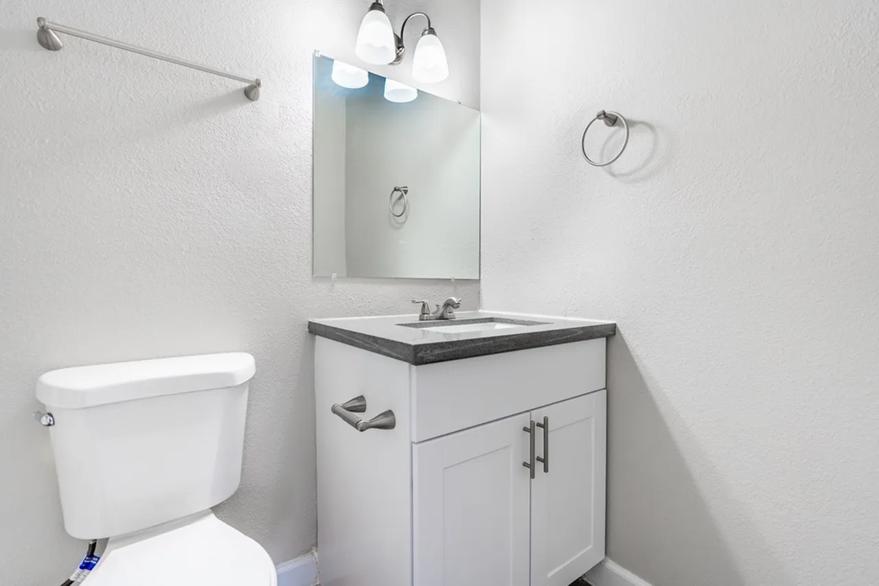 Bathroom, white vanity cabinetry, dark countertop, mirror with sconces