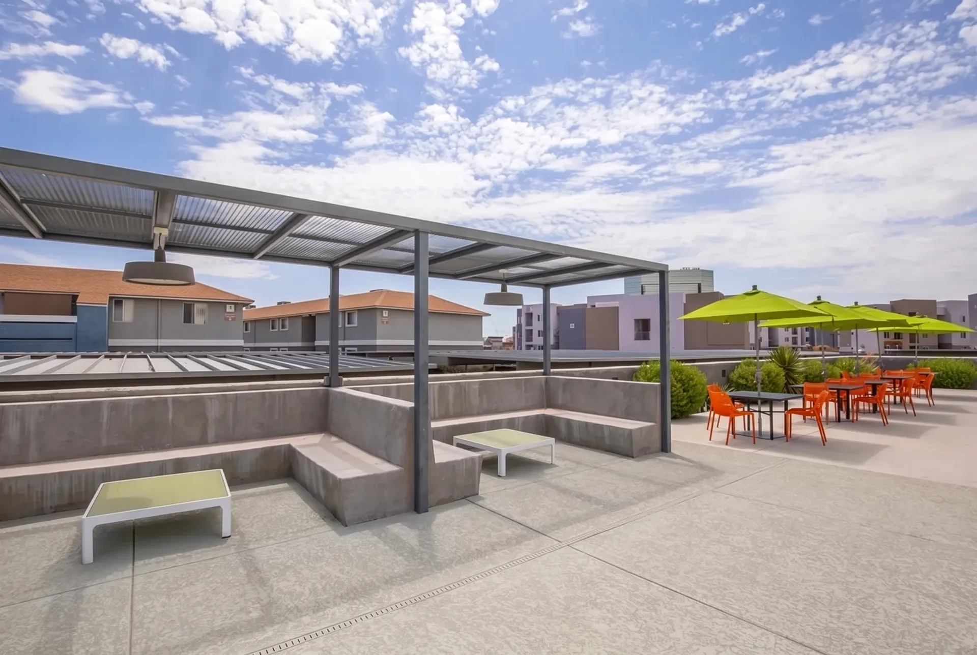Rooftop terrace with metal pergola, concrete seating, wood-style plank flooring, dining area with orange chairs, green shade umbrellas