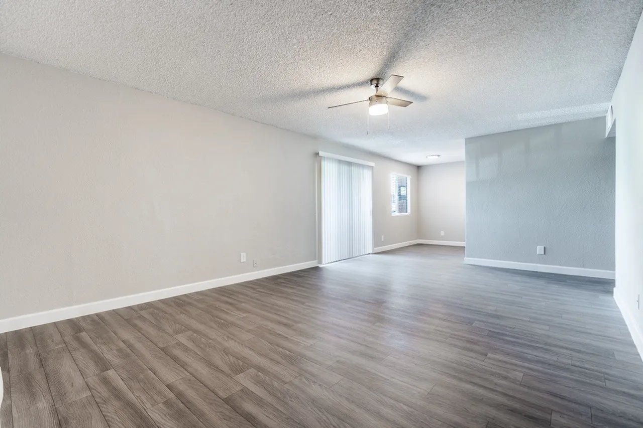 Living room, wood-style plank flooring, ceiling fan, neutral walls, sliding glass door
