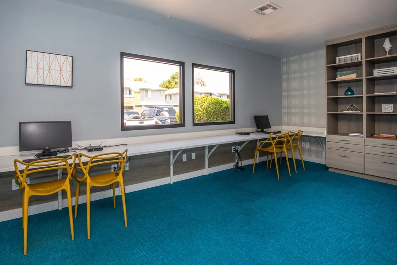 Business center, blue carpet flooring, built-in desk workspace, yellow mid-century chairs, windows