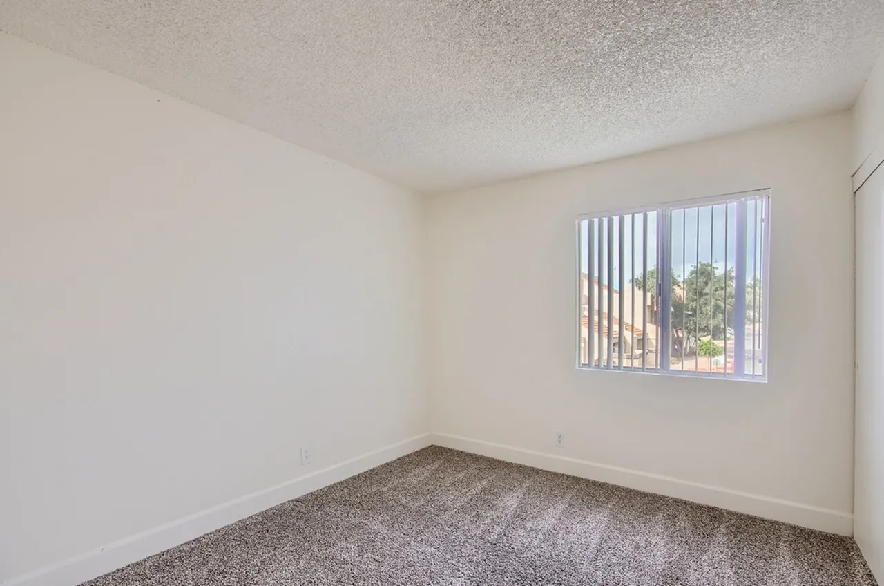 Bedroom, gray carpeting, textured ceiling, vertical blinds, natural light