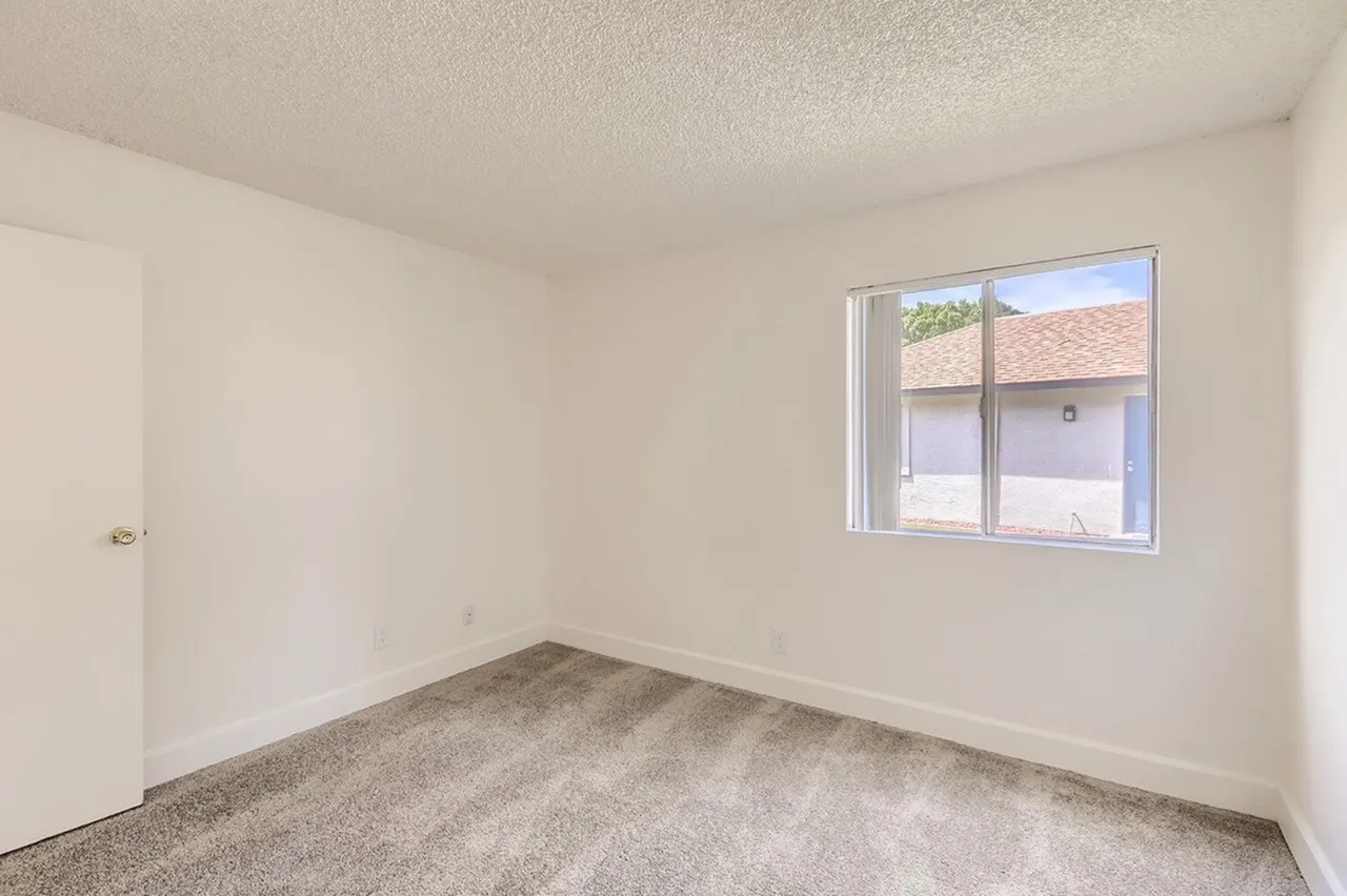Bedroom, gray carpet flooring, bright window, white walls, entry door