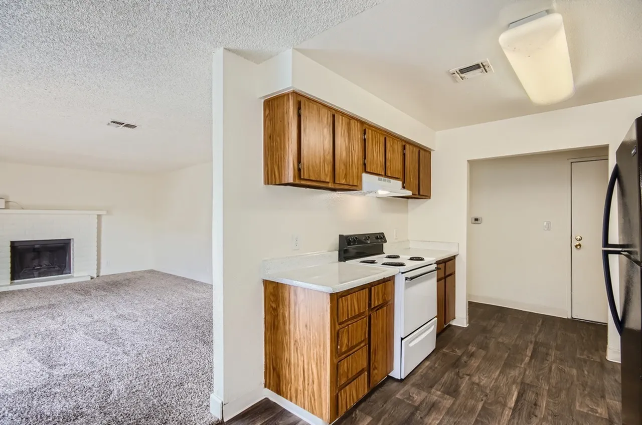 Kitchen with wood cabinetry, white electric range, white countertops, wood-style plank flooring, open to living room