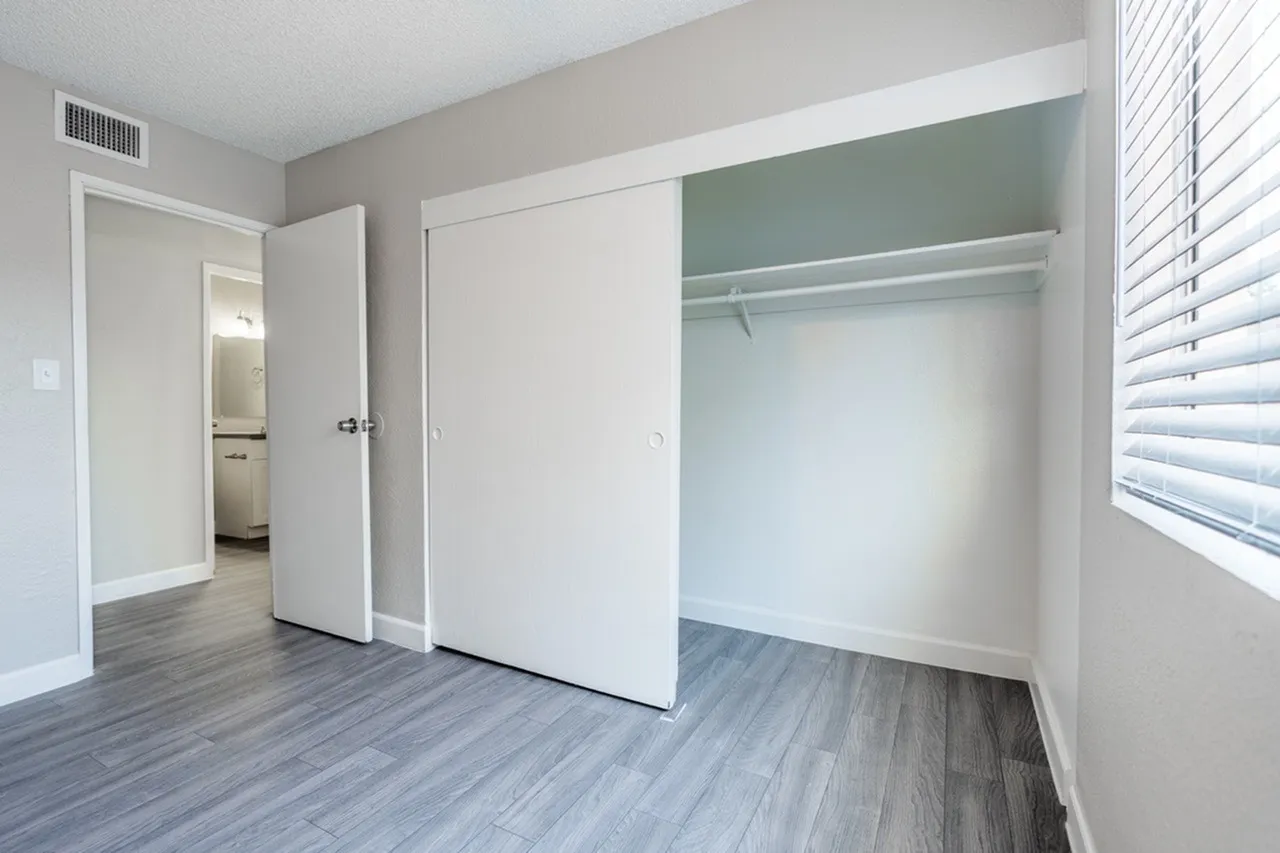 Bedroom, wood-style plank flooring, open closet with shelving, white doors, window blinds