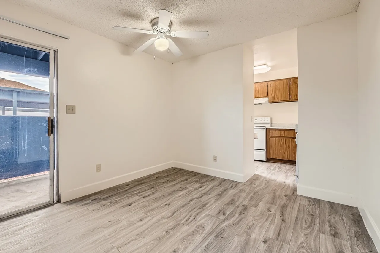 Living room, wood-style plank flooring, ceiling fan, glass entry door, open kitchen area