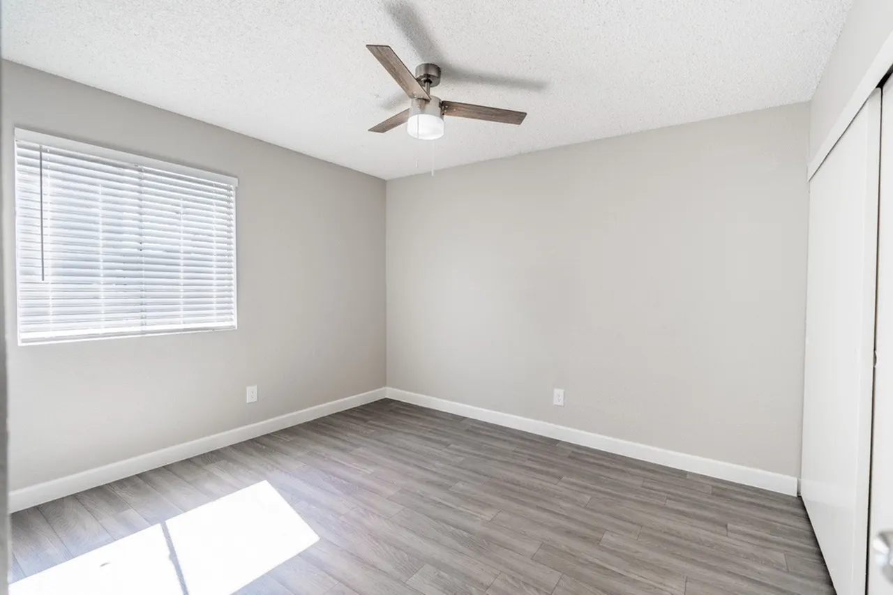 Bedroom, wood-style plank flooring, ceiling fan with light, beige walls, window with blinds