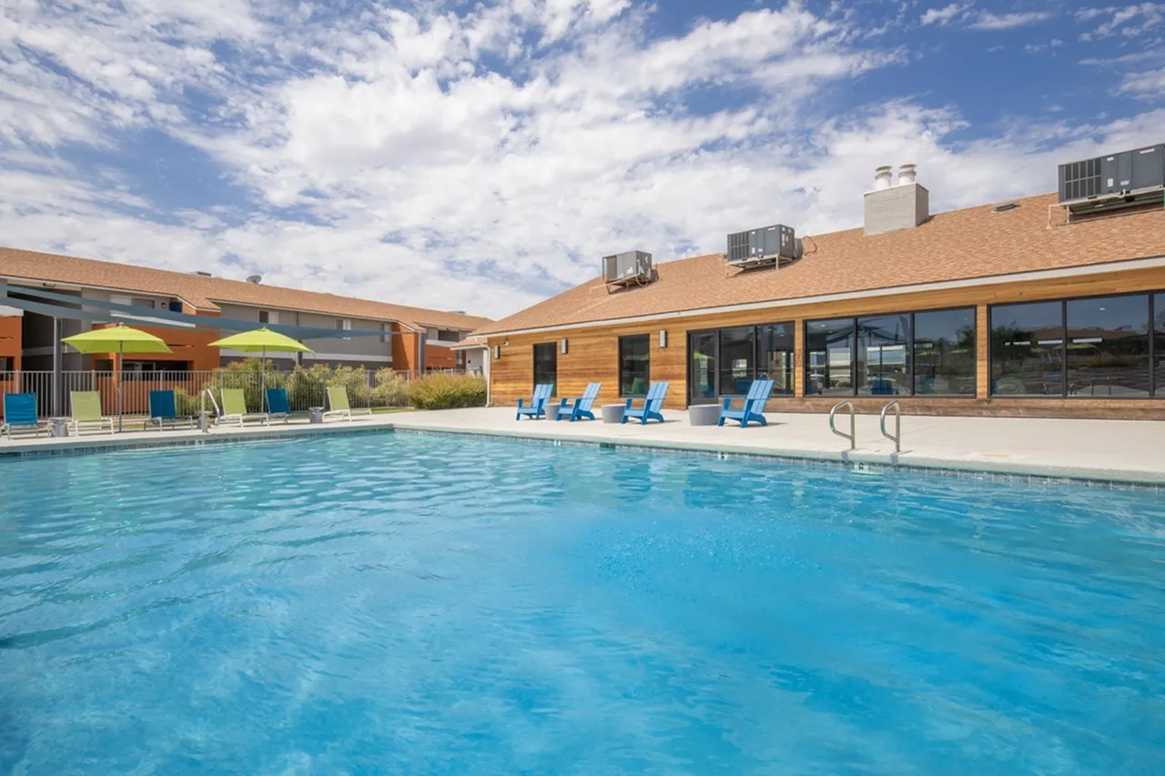 Outdoor swimming pool, lounge chairs, modern brick building, blue sky