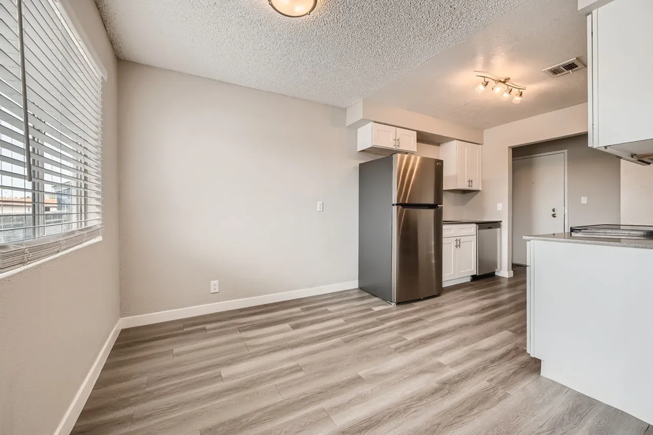 Kitchen with white cabinetry, stainless appliances, wood-style plank flooring, open to living space
