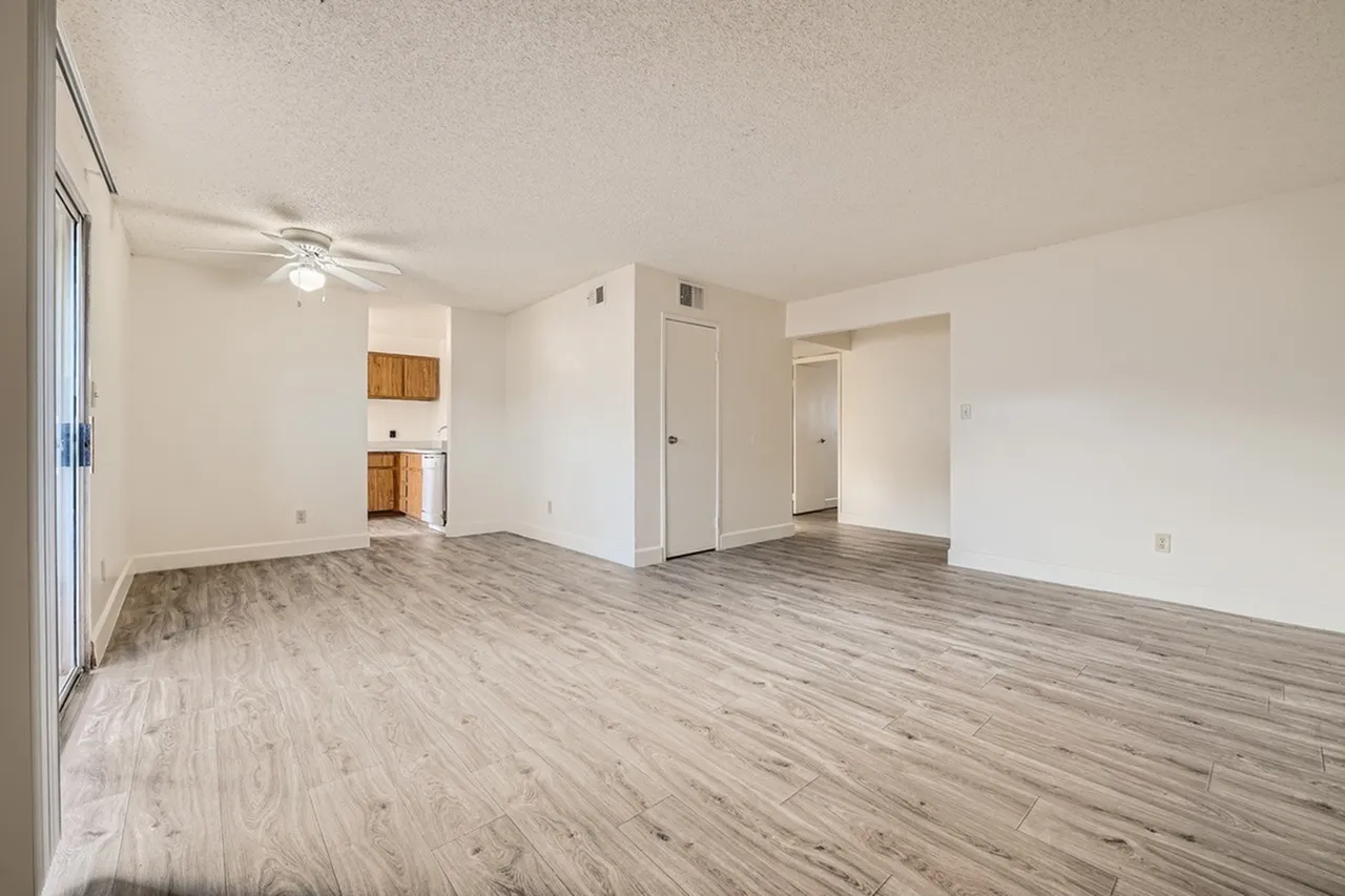 Living room, wood-style plank flooring, ceiling fan, white walls, entry doors