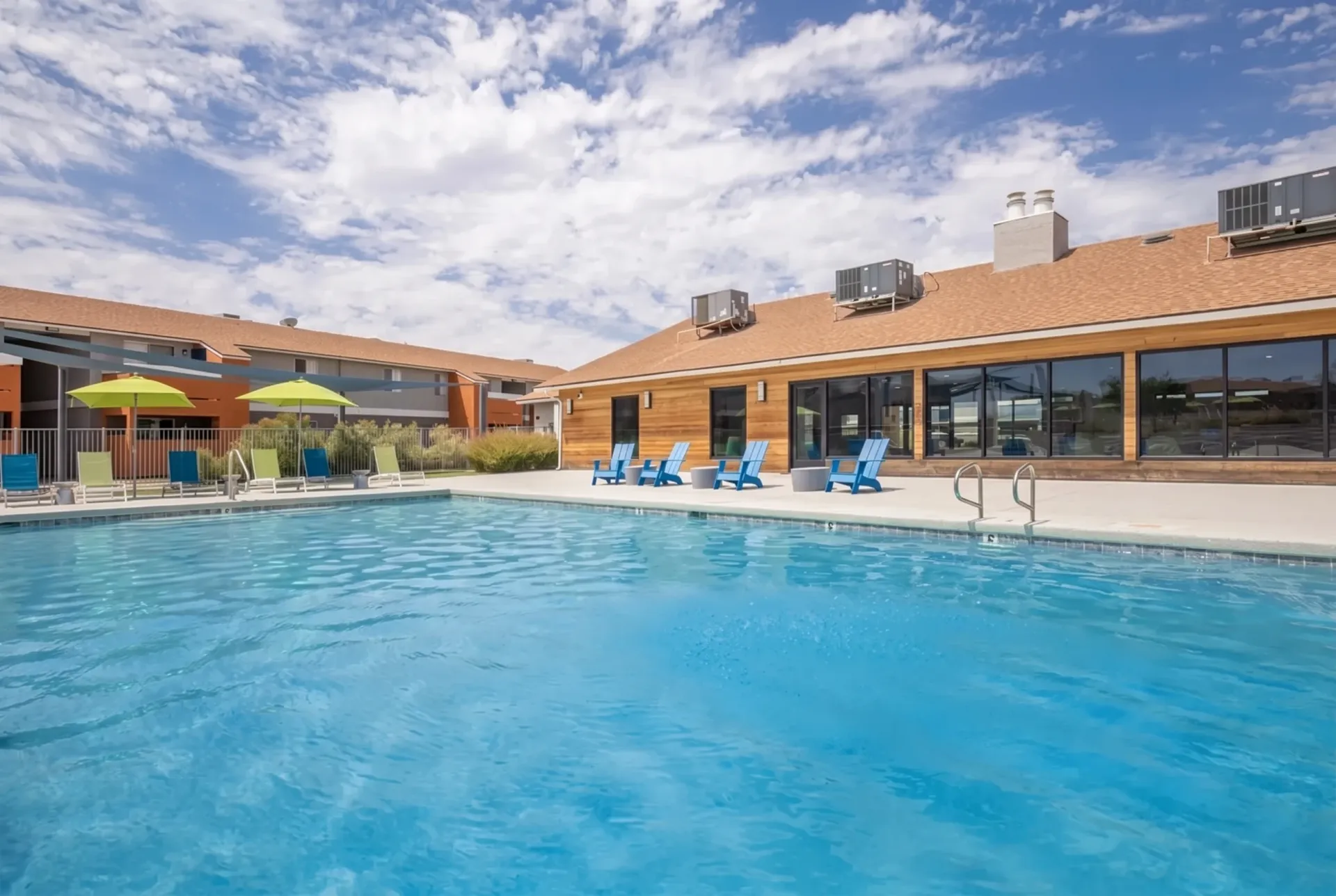 Outdoor swimming pool, lounge chairs, modern brick building, blue sky