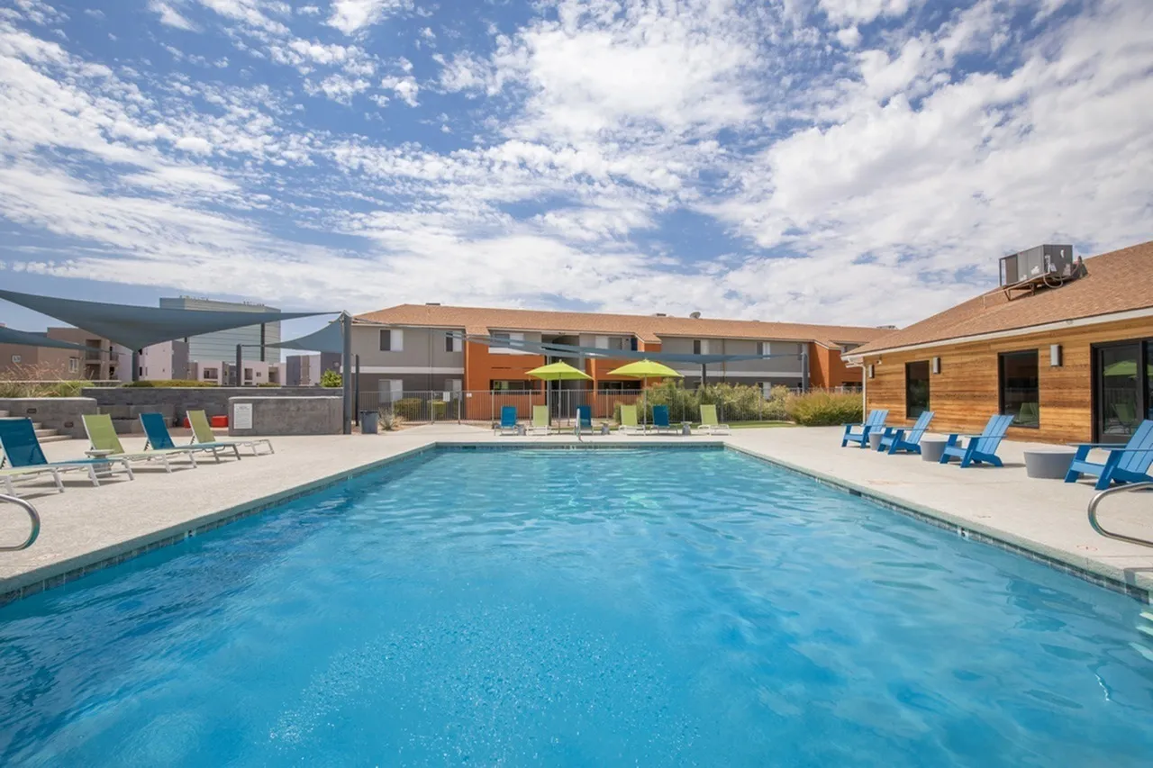Resort-style swimming pool, blue umbrellas, lounge chairs, wood-style building, patio