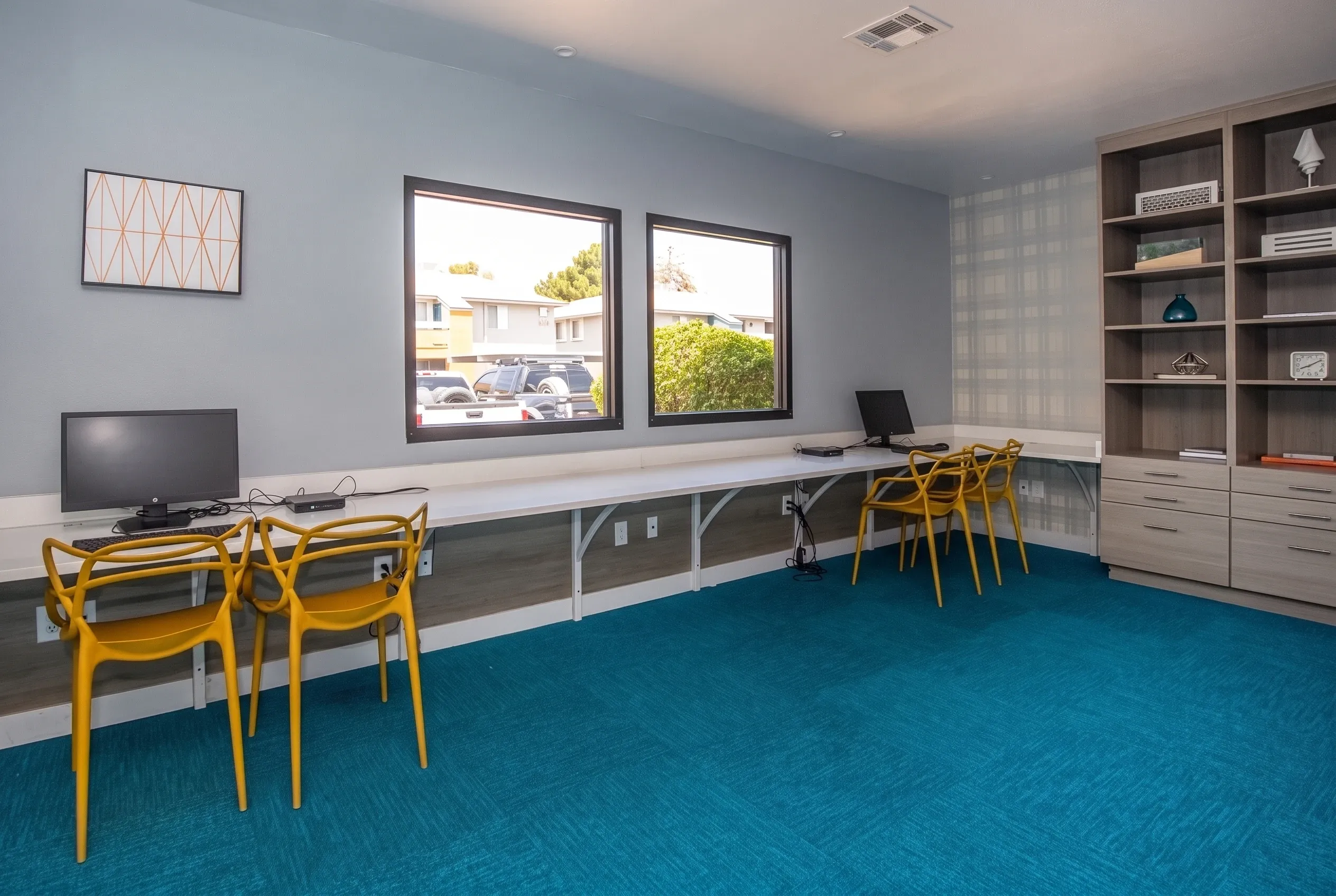 Business center, blue carpet flooring, built-in desk workspace, yellow mid-century chairs, windows