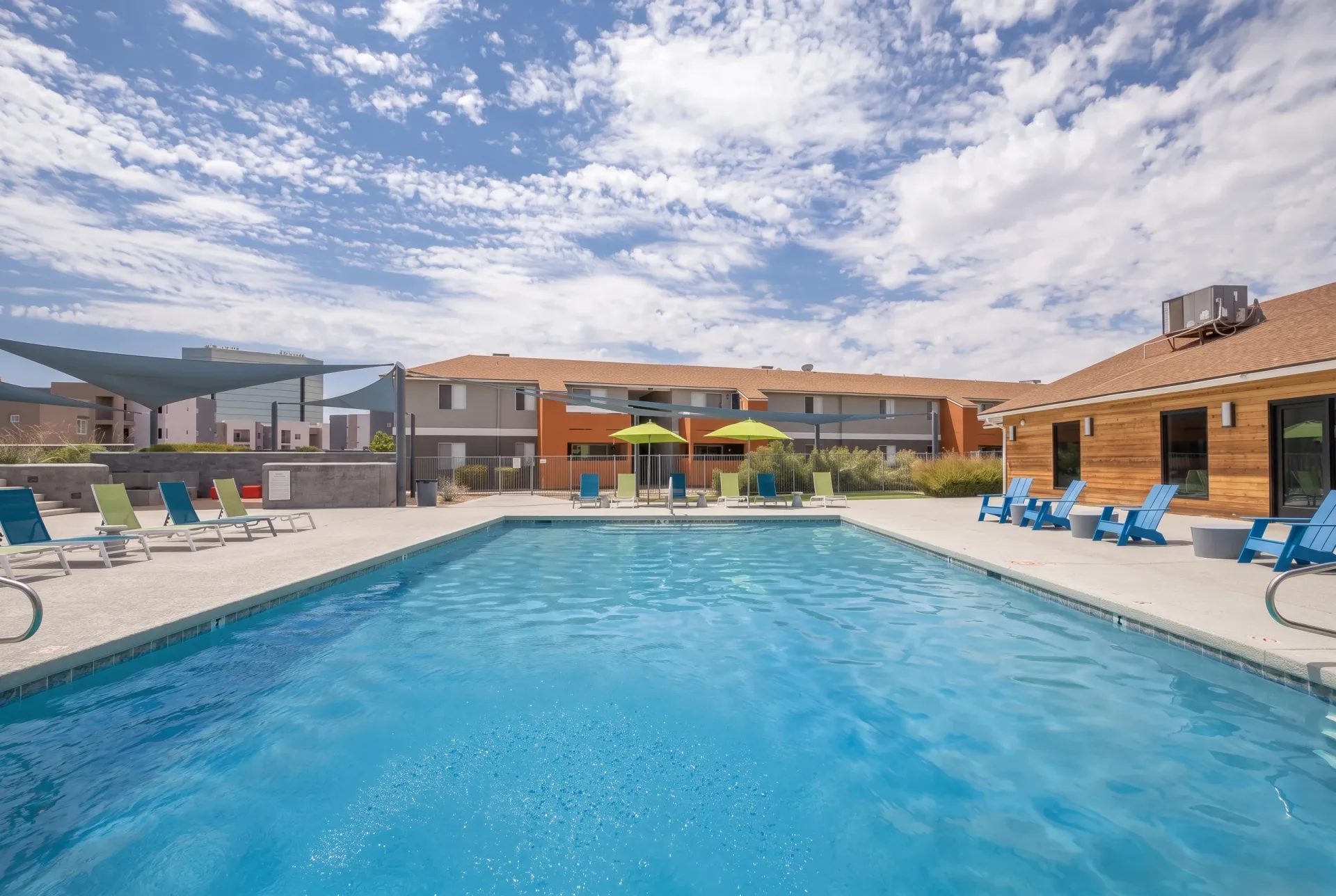 Resort-style swimming pool, blue umbrellas, lounge chairs, wood-style building, patio