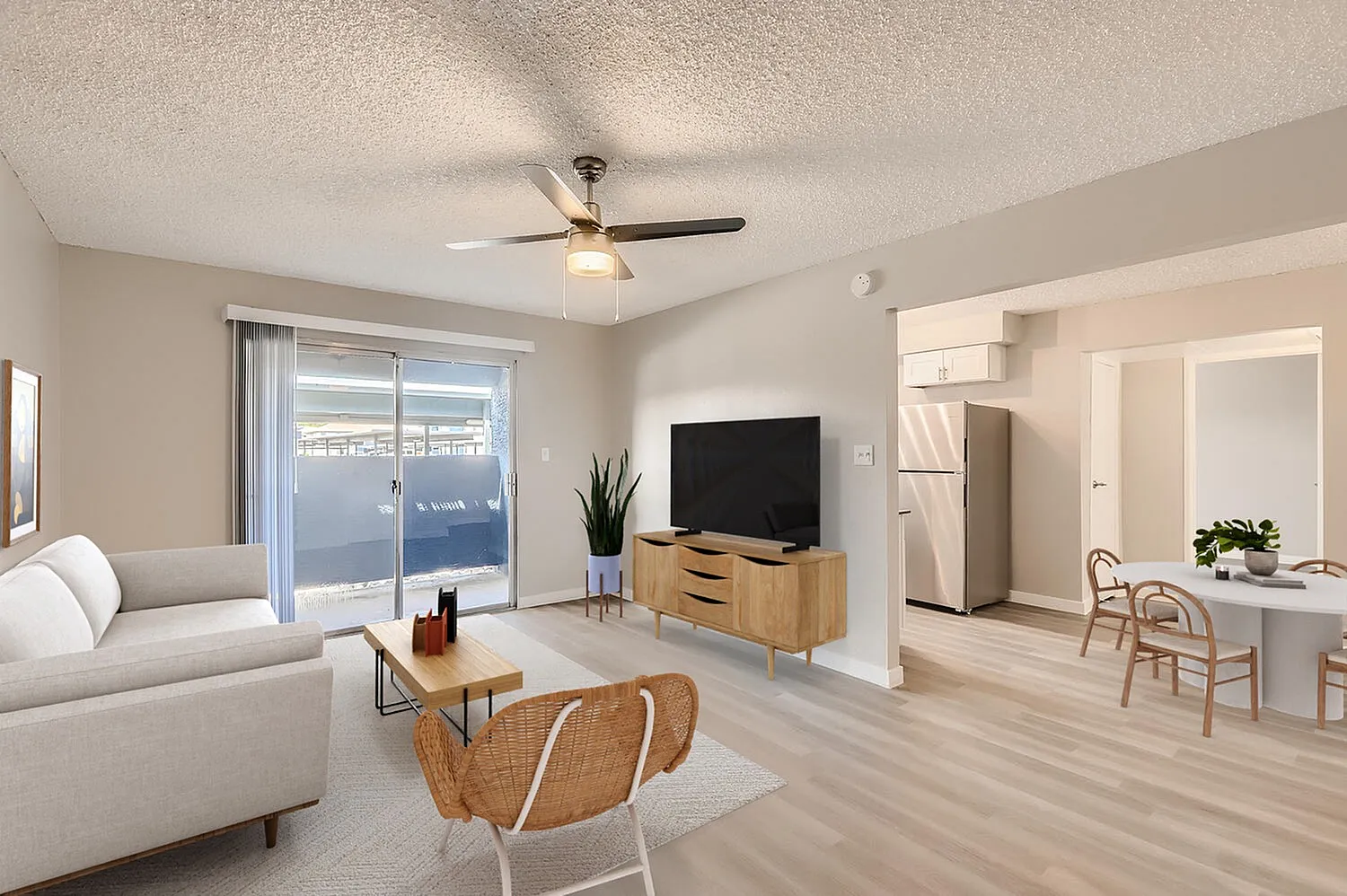 Living room with wood-style plank flooring, ceiling fan, gray sofa, coffee table, kitchen with white cabinetry and dining area