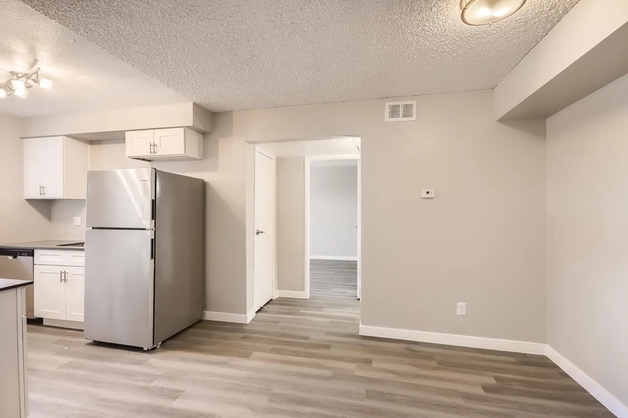 Kitchen and living space, white cabinetry, stainless steel refrigerator, wood-style plank flooring, open concept layout