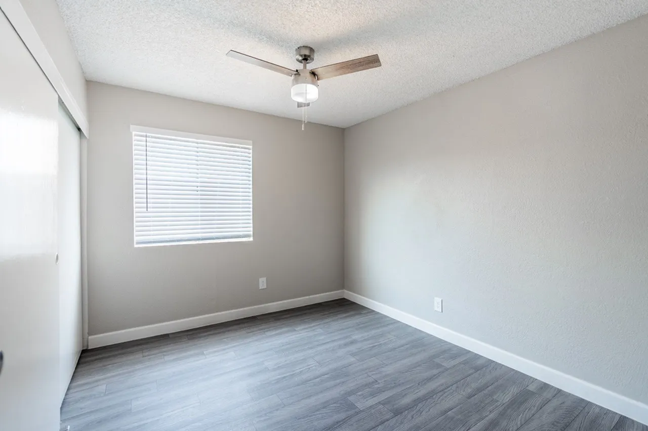 Bedroom, wood-style plank flooring, ceiling fan with light fixture, window with blinds
