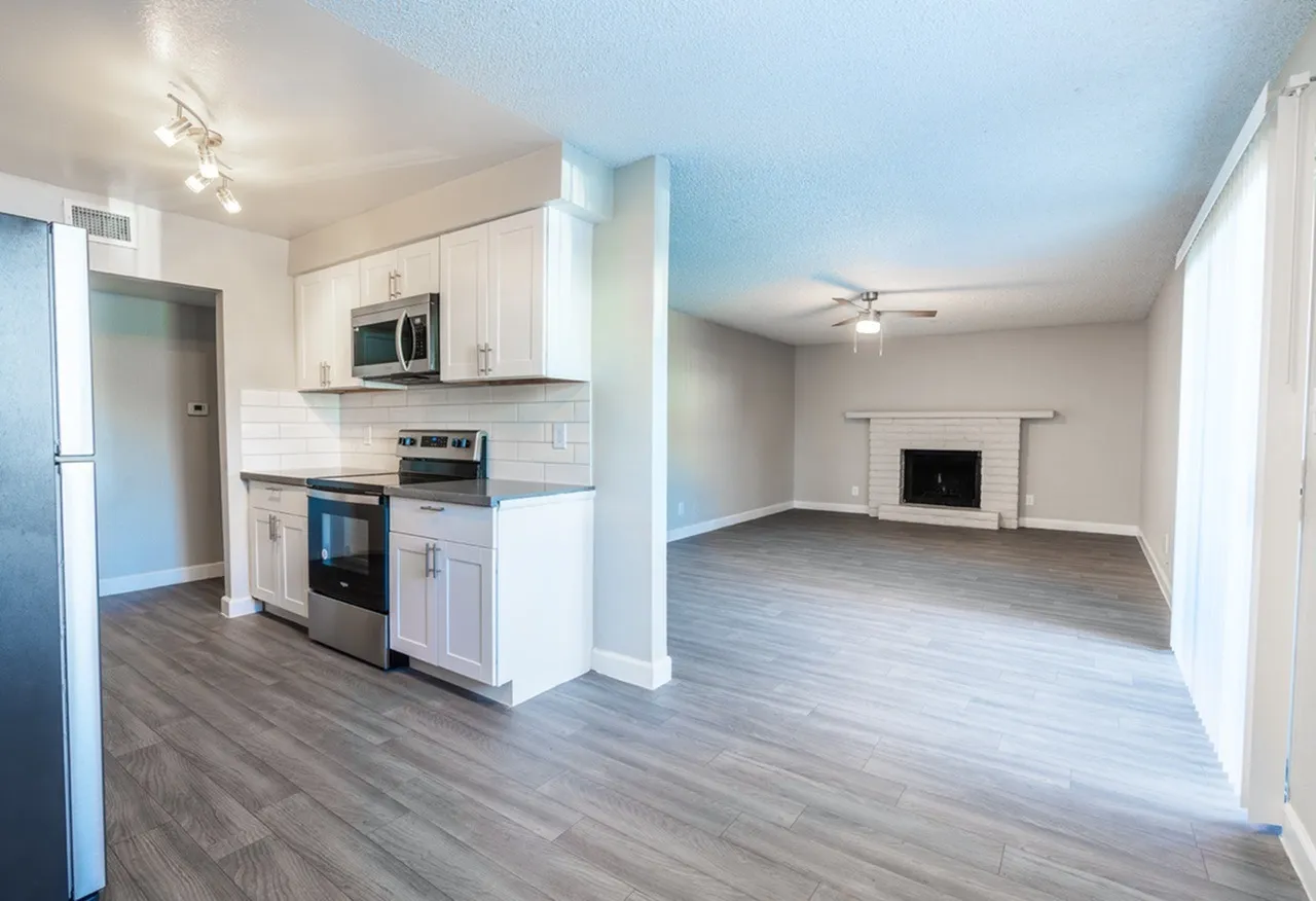 Kitchen, white shaker cabinetry, stainless appliances, subway tile backsplash, wood-style plank flooring, open living room with fireplace