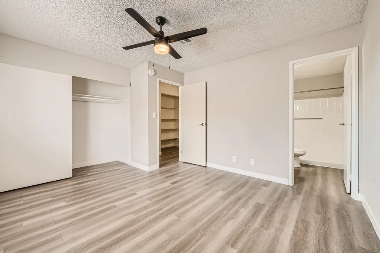 Primary bedroom, wood-style plank flooring, ceiling fan with light, walk-in closet, ensuite bathroom