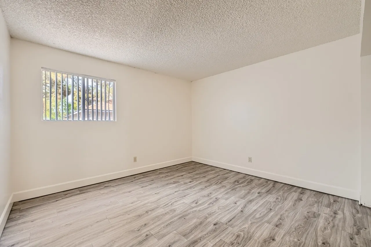 Empty bedroom, wood-style plank flooring, barred window with view, textured ceiling