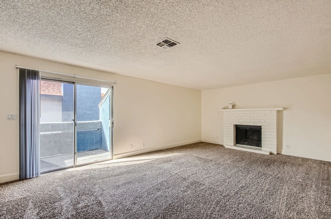 Living room, gray carpeting, fireplace with surround, sliding glass door to balcony