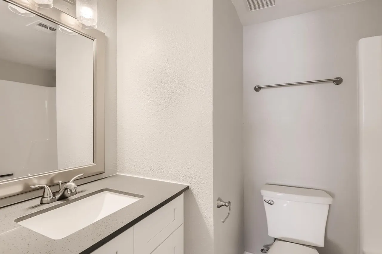 Bathroom, white vanity with undermount sink, brushed nickel hardware, toilet, shower towel bar