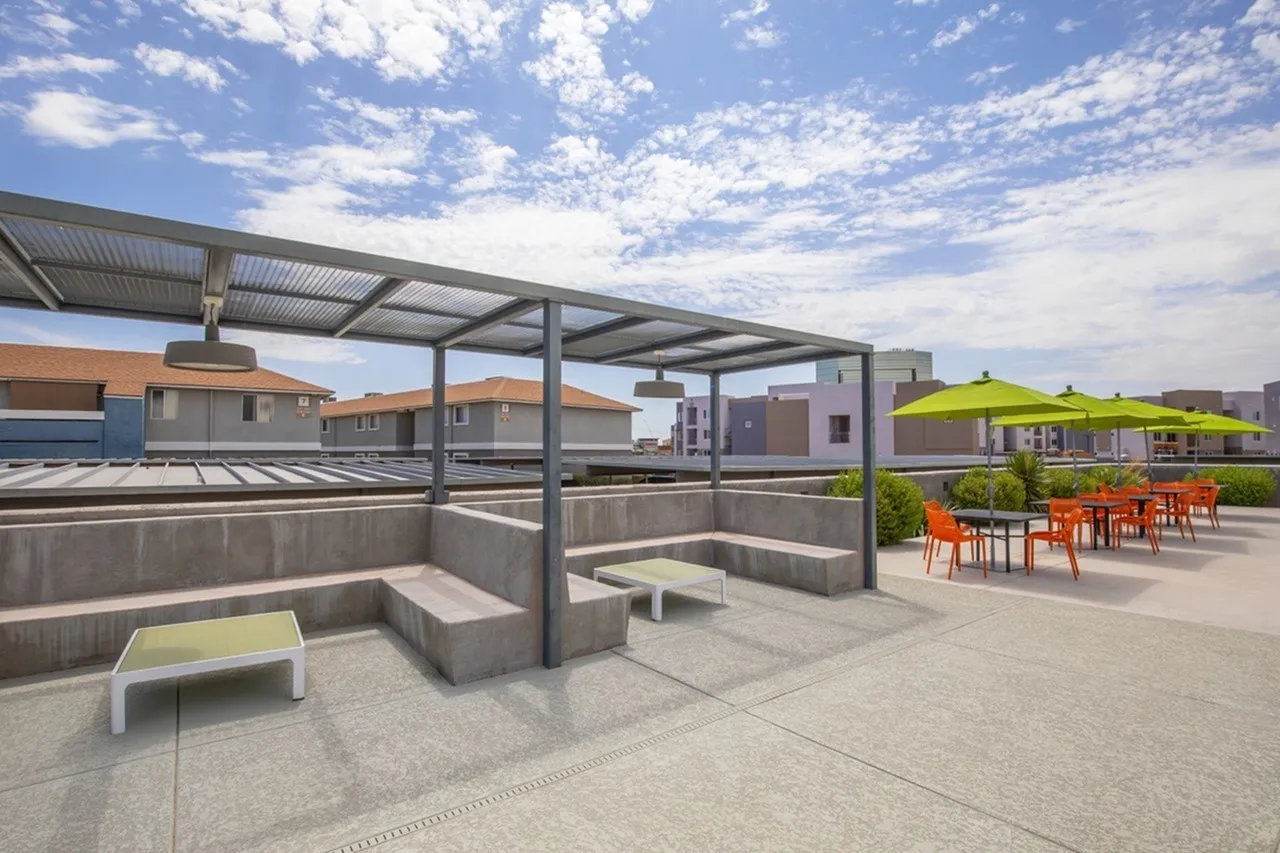 Rooftop terrace with metal pergola, concrete seating, wood-style plank flooring, dining area with orange chairs, green shade umbrellas