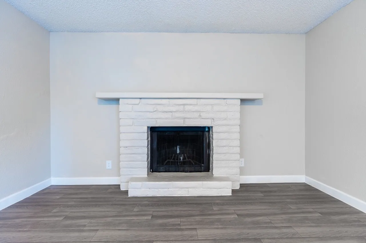 Living room, wood-style plank flooring, white brick fireplace surround, black fireplace insert, blue floating shelf