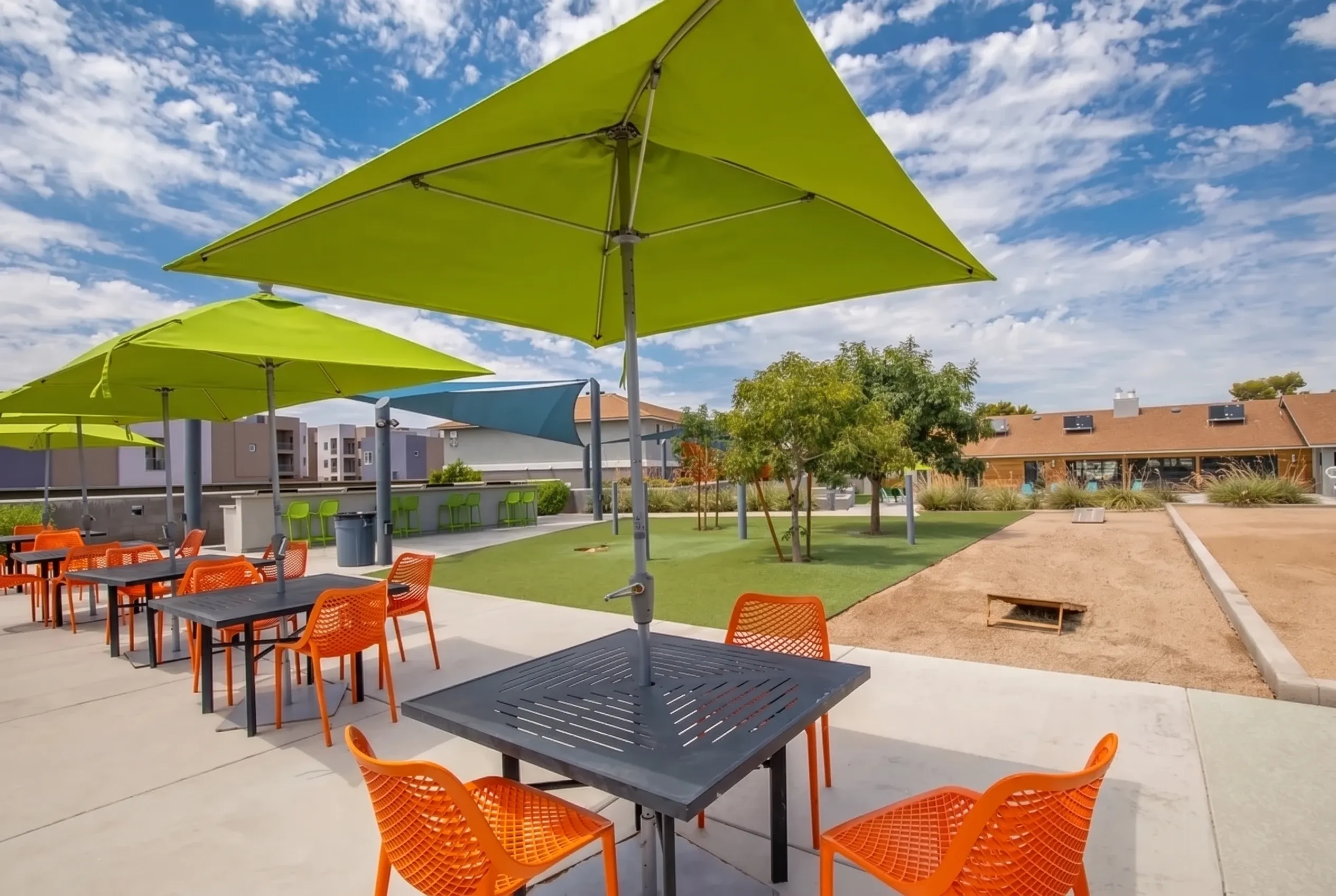 Patio with lime green umbrellas, orange metal chairs, dark tables, green lawn, modern buildings