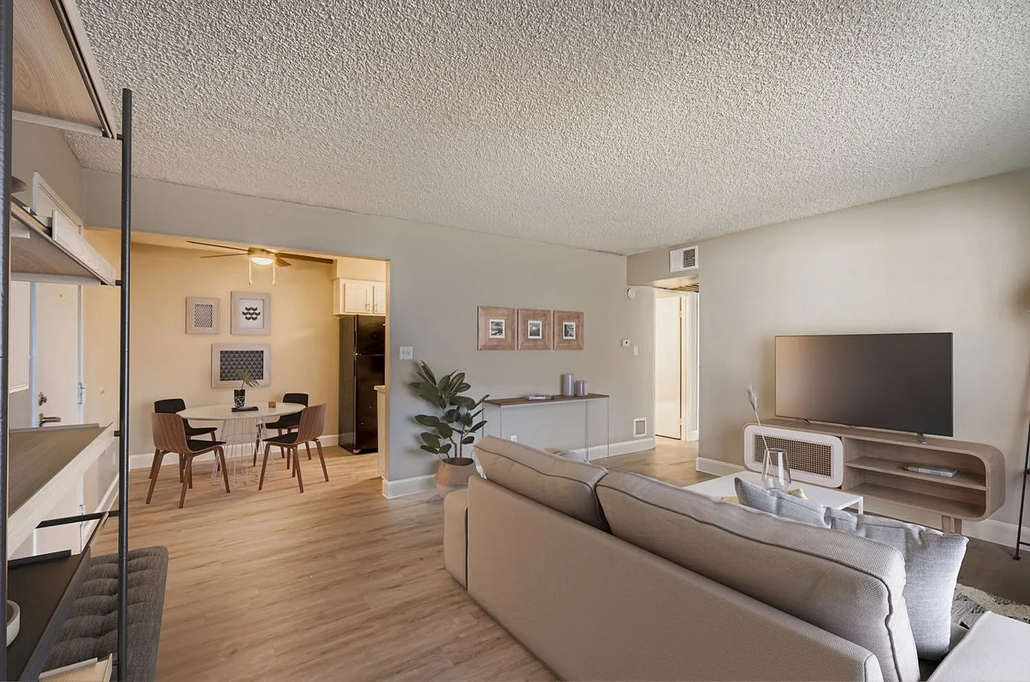 Living room with wood-style plank flooring, gray sofa, ceiling fan, dining table visible through opening