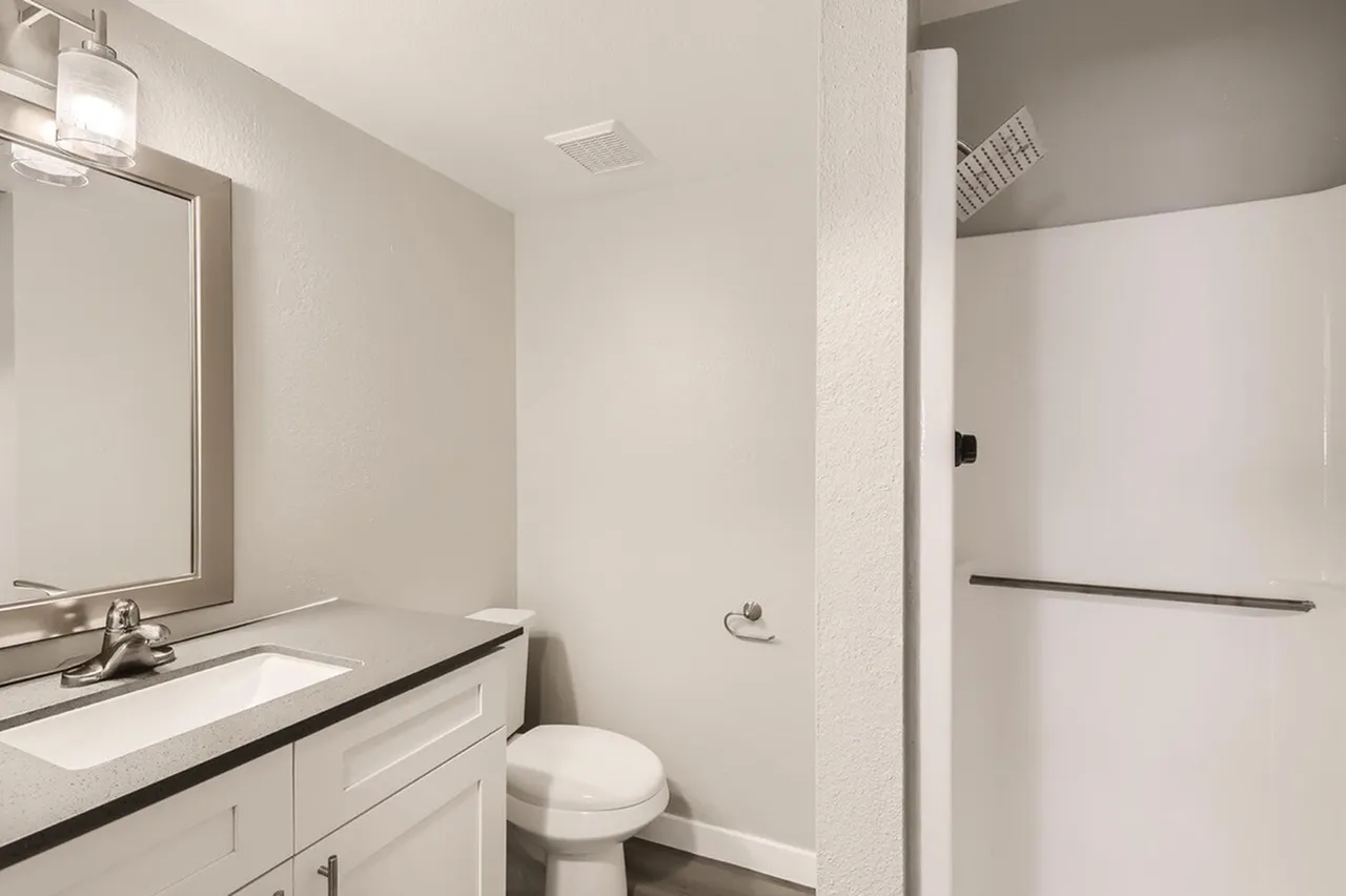Bathroom, white cabinetry, quartz countertop, framed mirror, glass shower enclosure