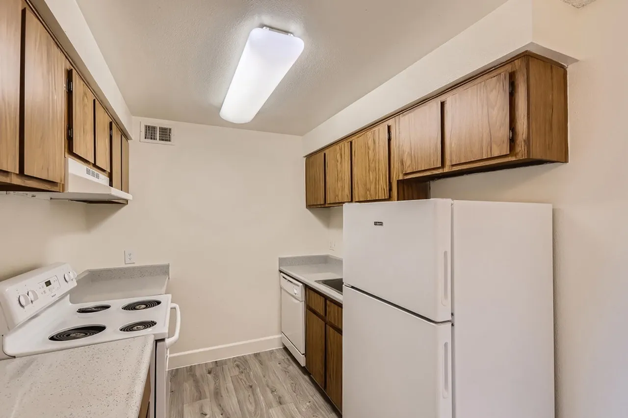 Kitchen, wood cabinetry, white appliances, wood-style plank flooring, fluorescent ceiling light