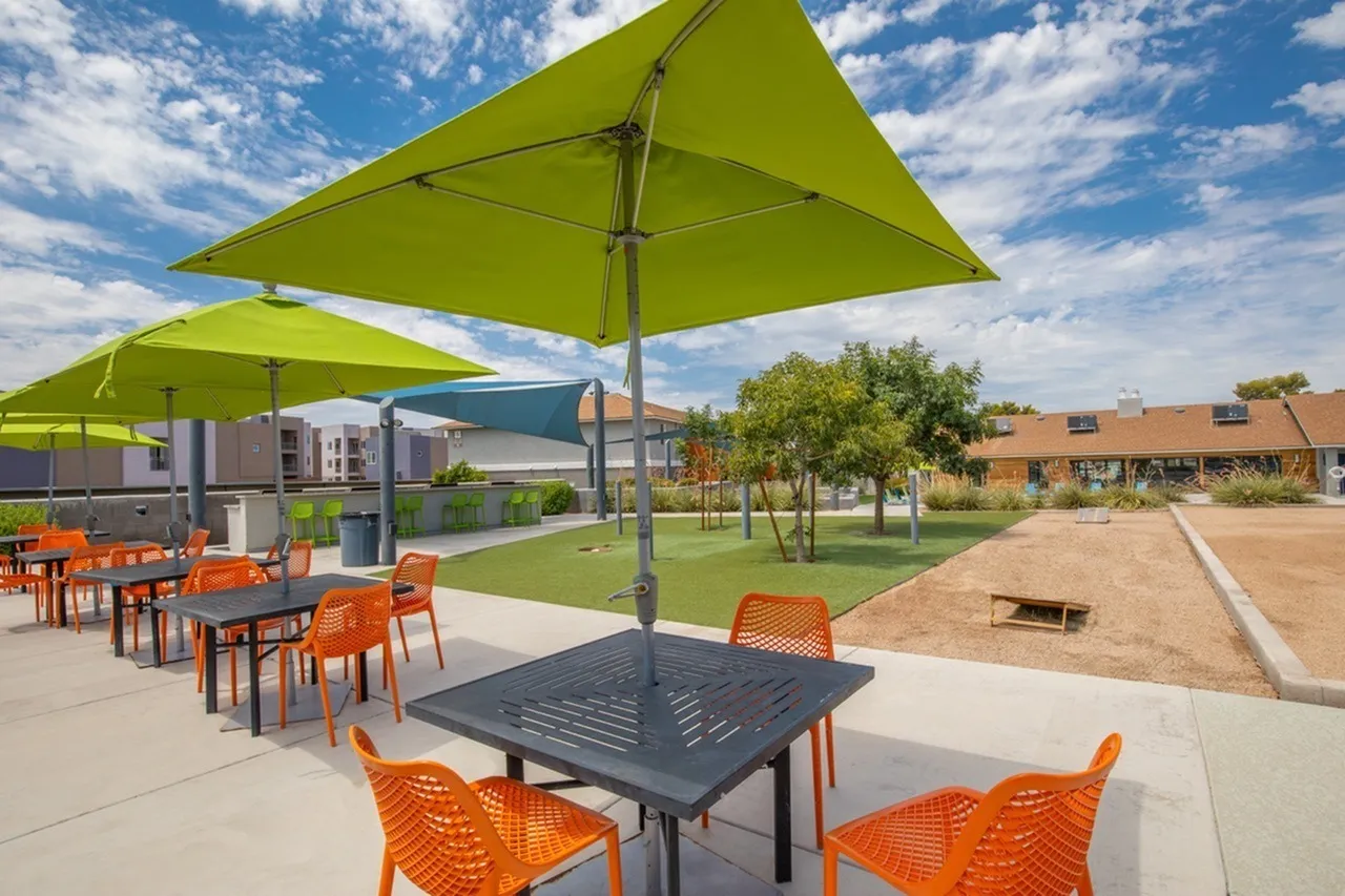 Patio with lime green umbrellas, orange metal chairs, dark tables, green lawn, modern buildings