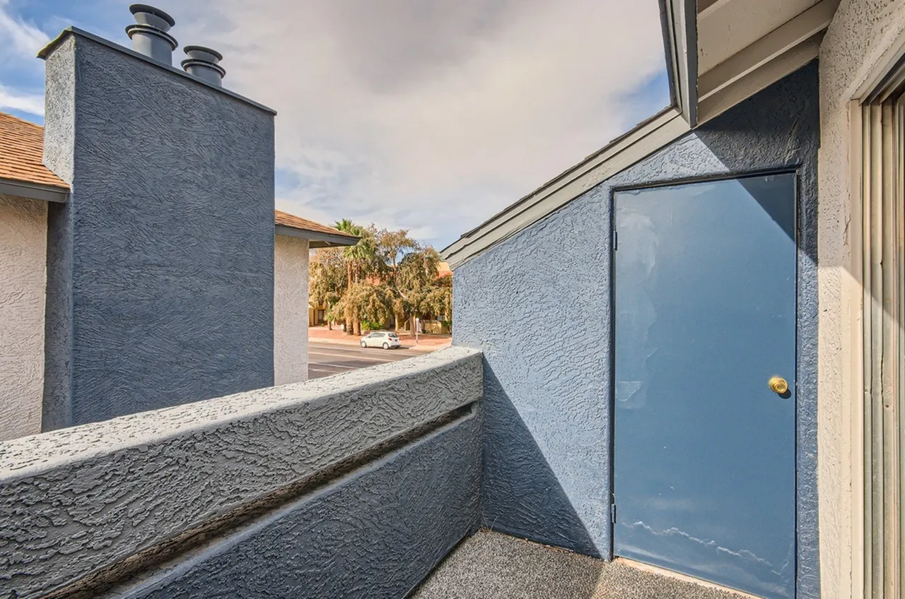 Courtyard with blue-gray textured walls, blue door, chimney structures, wood-style landscaping