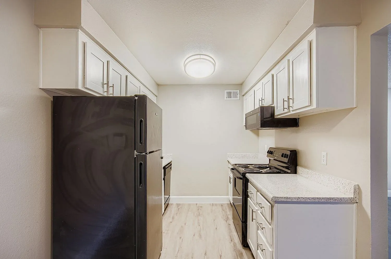 Kitchen, white cabinetry, gray countertops, black appliances, wood-style plank flooring