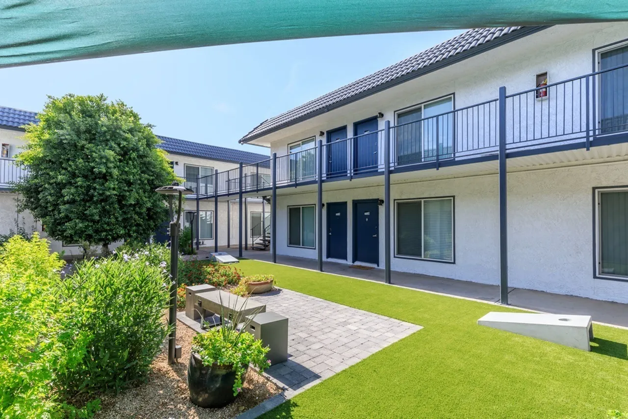 Courtyard with manicured lawn, patio seating, metal railings, blue shade structure