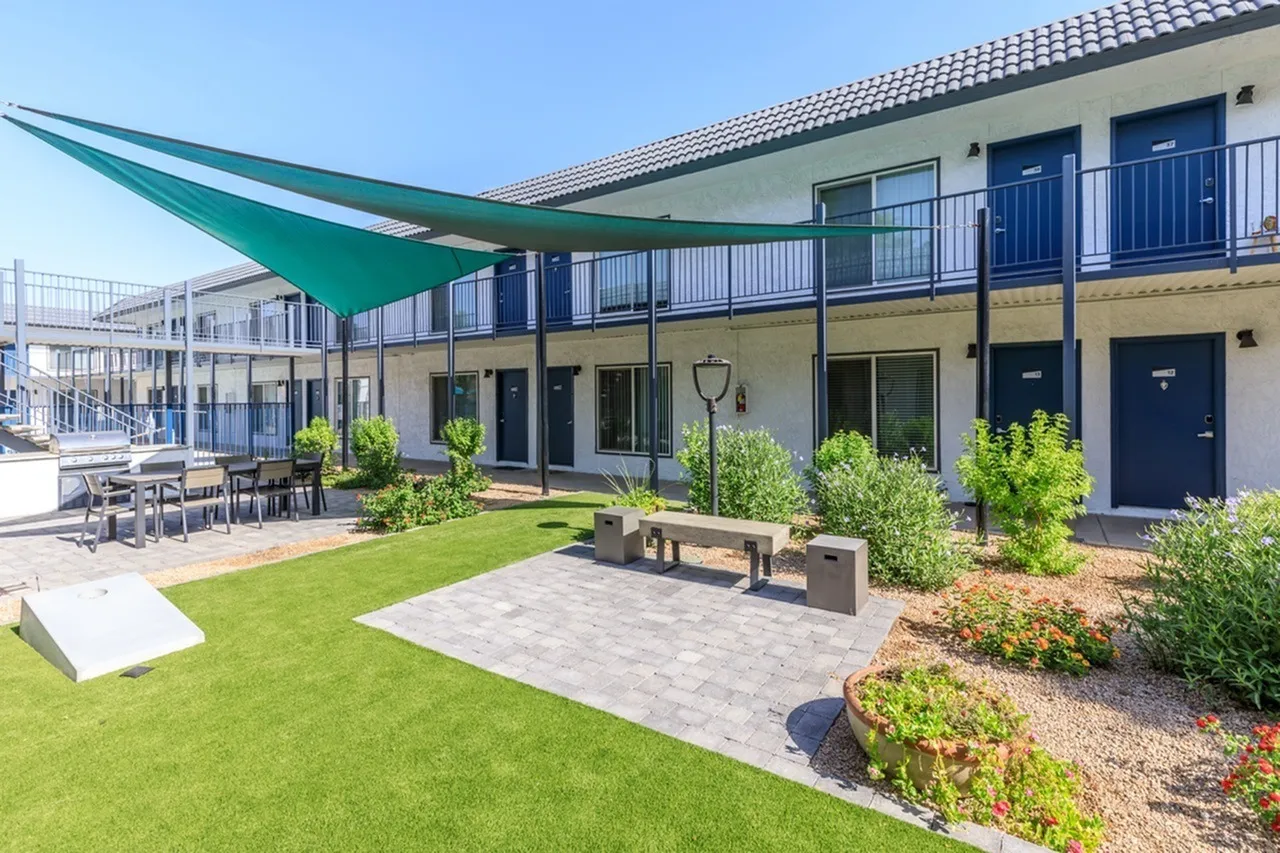 Courtyard with green shade sail, lawn seating area, concrete patio, raised planters, multi-story building