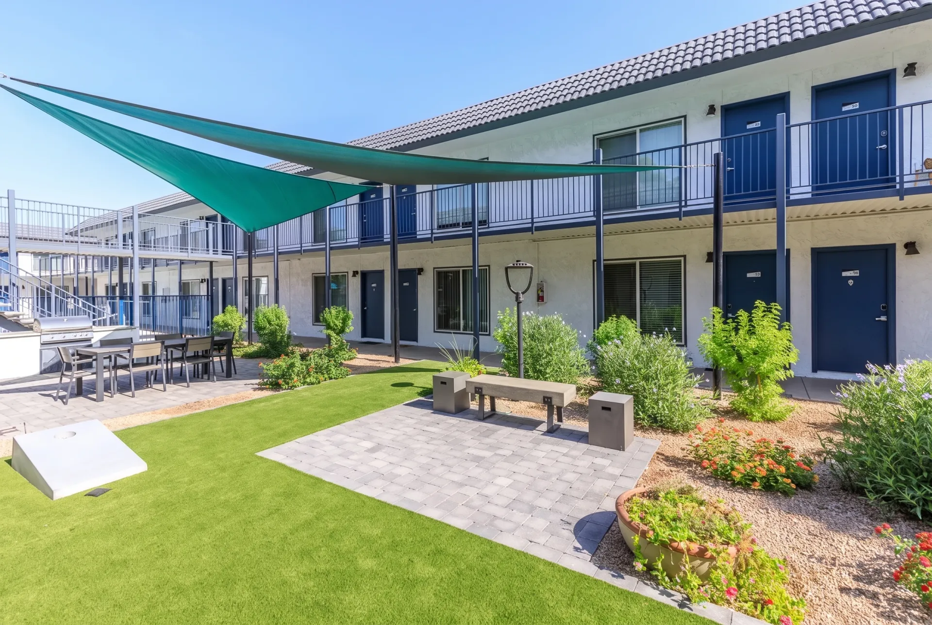 Courtyard with green shade sail, lawn seating area, concrete patio, raised planters, multi-story building