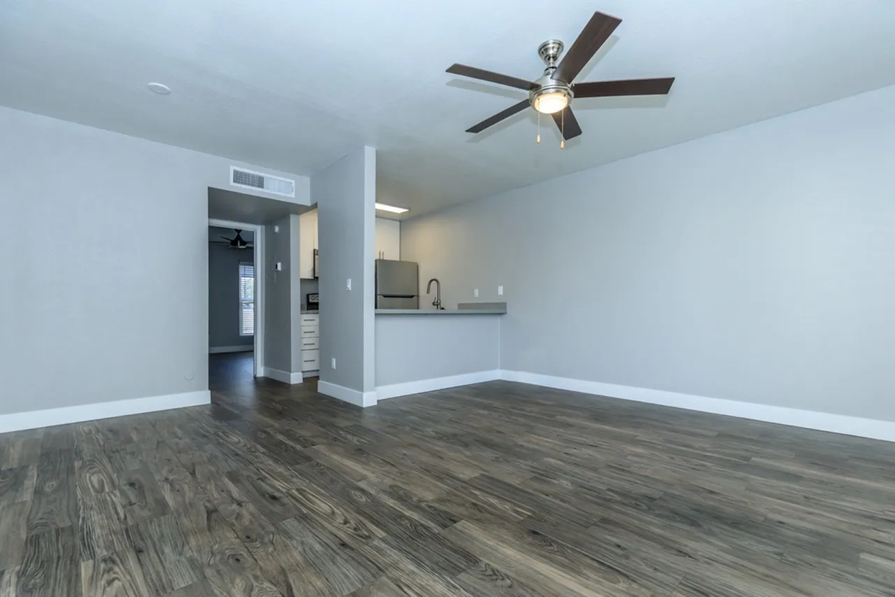 Open living area, wood-style plank flooring, ceiling fan, kitchen with appliances