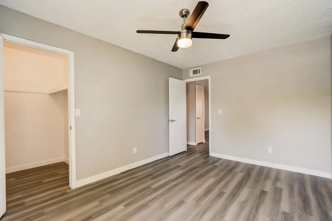 Primary bedroom, wood-style plank flooring, ceiling fan, closet and doors